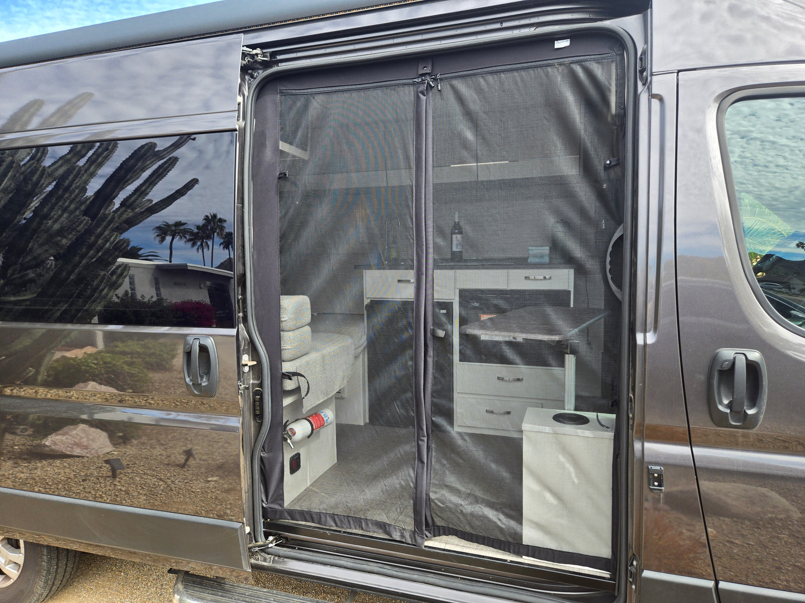 RV rental: sliding door open, magnetic screen reveals organized interior with kitchen, seating, and fire extinguisher. Ready for adventure.