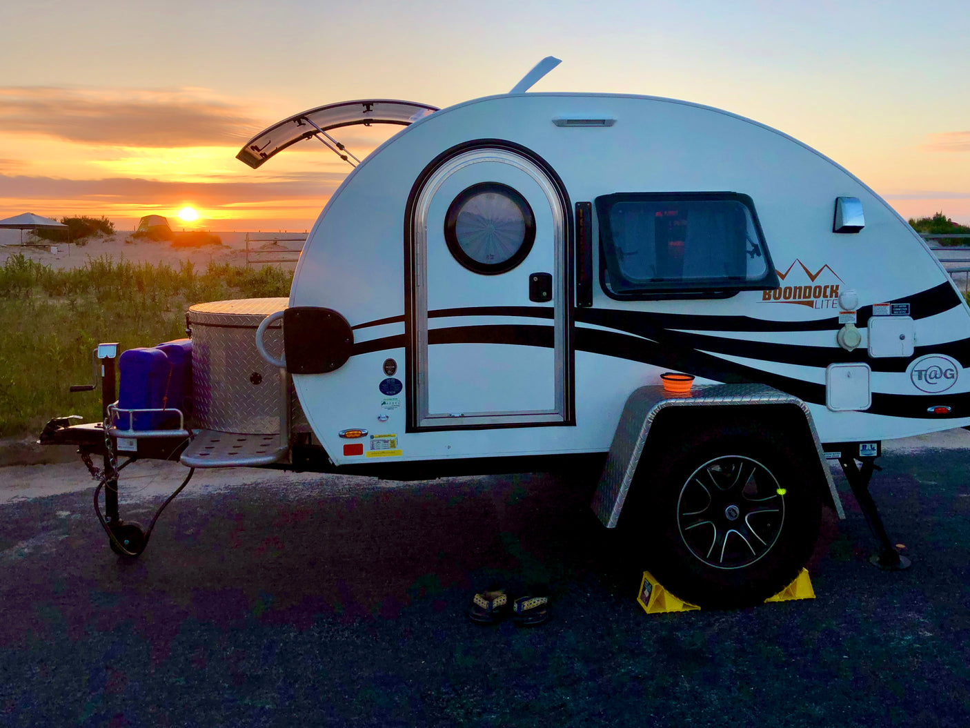 White teardrop RV rental enjoying a serene sunset over sandy dunes. Perfect for a cozy camping getaway.