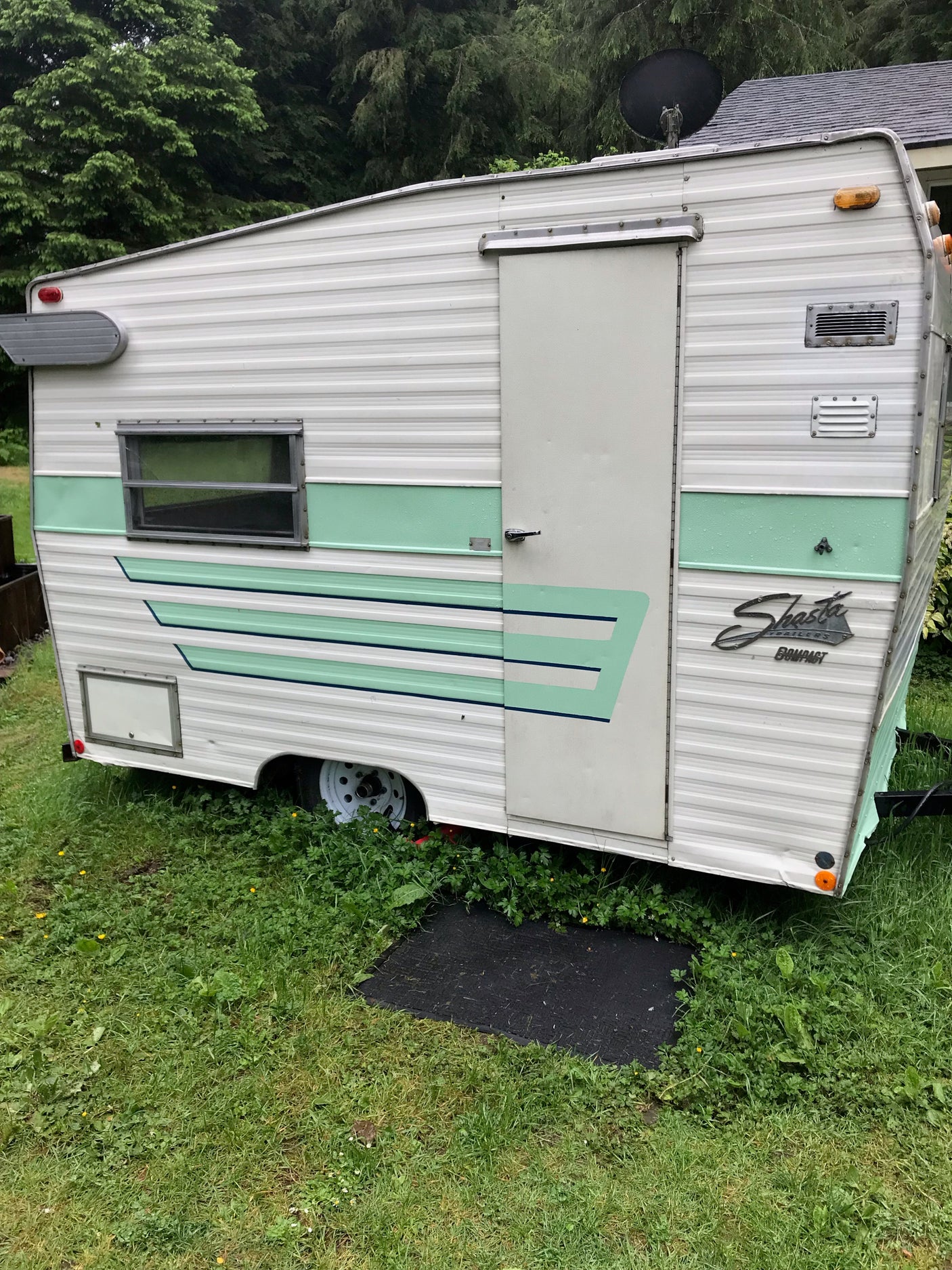 A charming vintage Shasta Compact travel trailer, in white and green, sits on grass, ready for an RV rental.