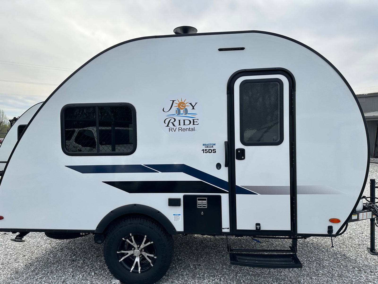 Side view of a white Braxton Creek 15DS travel trailer for RV rental, featuring the "Joy Ride" logo.