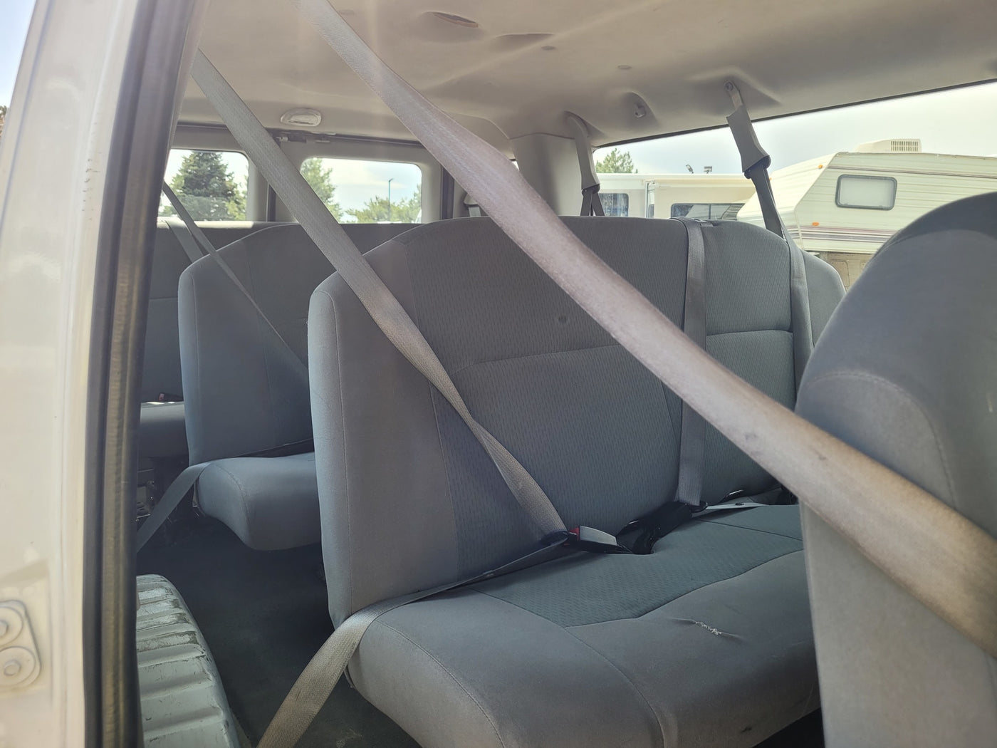 View from inside a passenger van with grey seats and seatbelts, offering a glimpse of an RV rental in the background. — photo 3