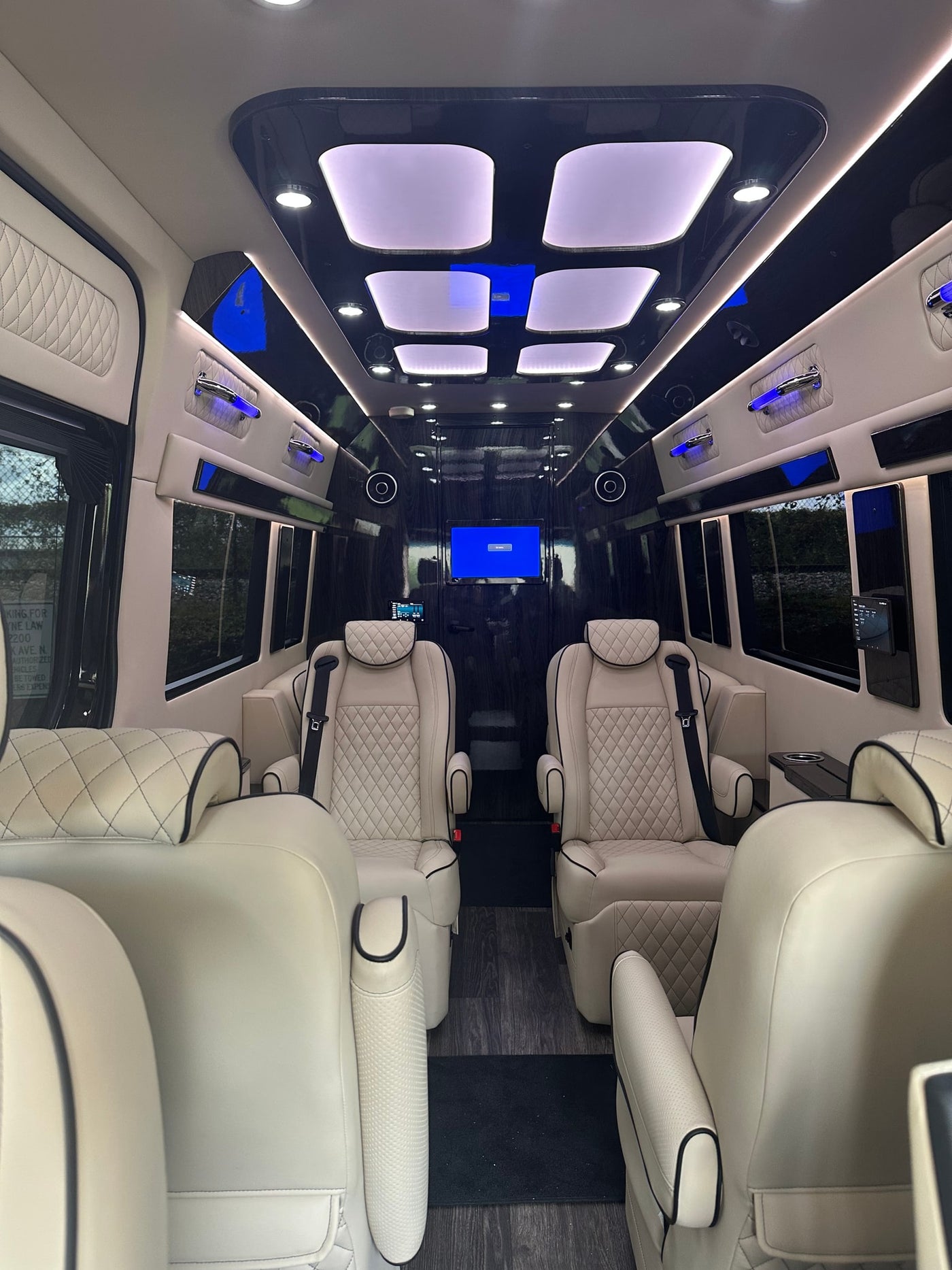 its reflective surface shows trees & sky.|A glossy black Mercedes Sprinter van — photo 6