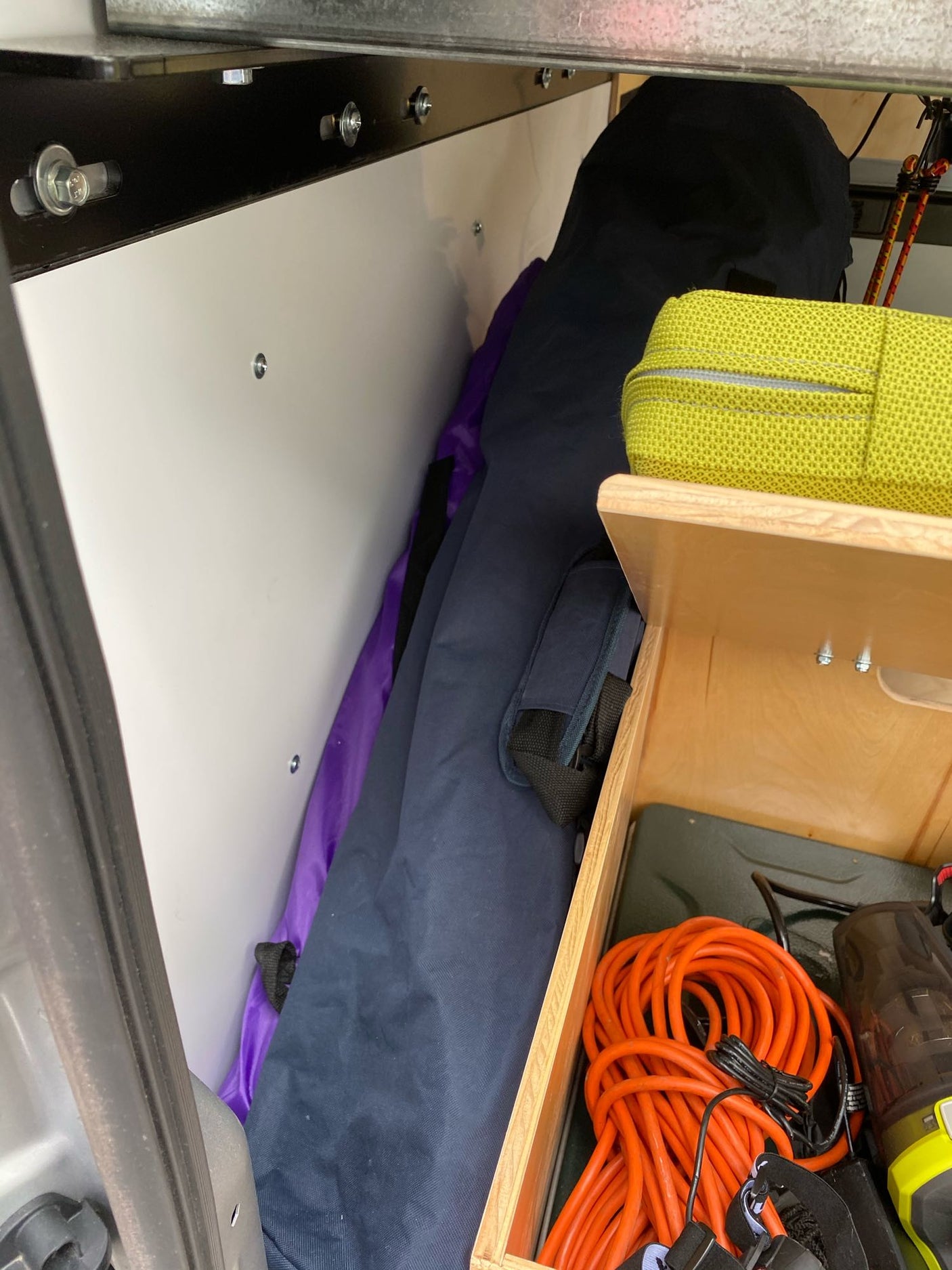 Organized RV rental interior storage with a bright yellow bag, coiled orange power cord, and essential tools.