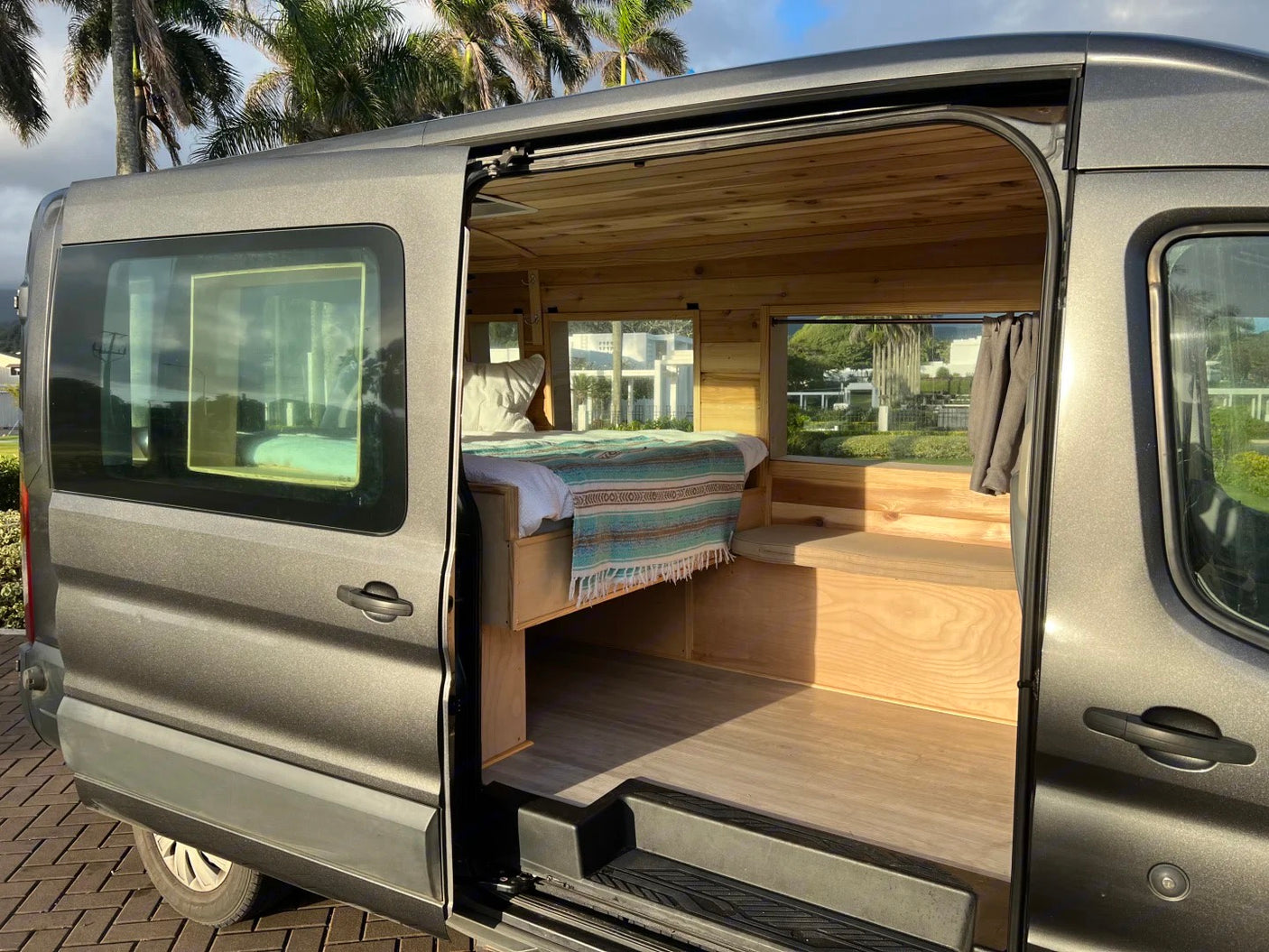 Gray rv rental camper van with open door revealing a custom wood interior, comfy bed, and bright windows for travel.