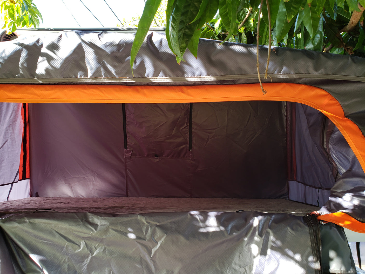 Inside a comfortable RV rental rooftop tent, featuring grey fabric walls, orange accents, and a sleeping platform.