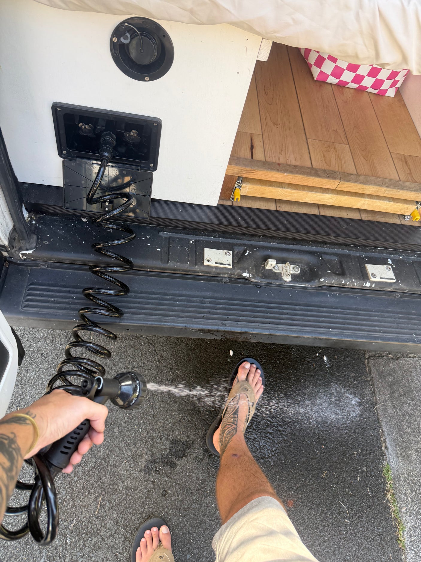 An RV rental's external shower in use. A person sprays water from a coiled hose, perfect for outdoor cleaning.