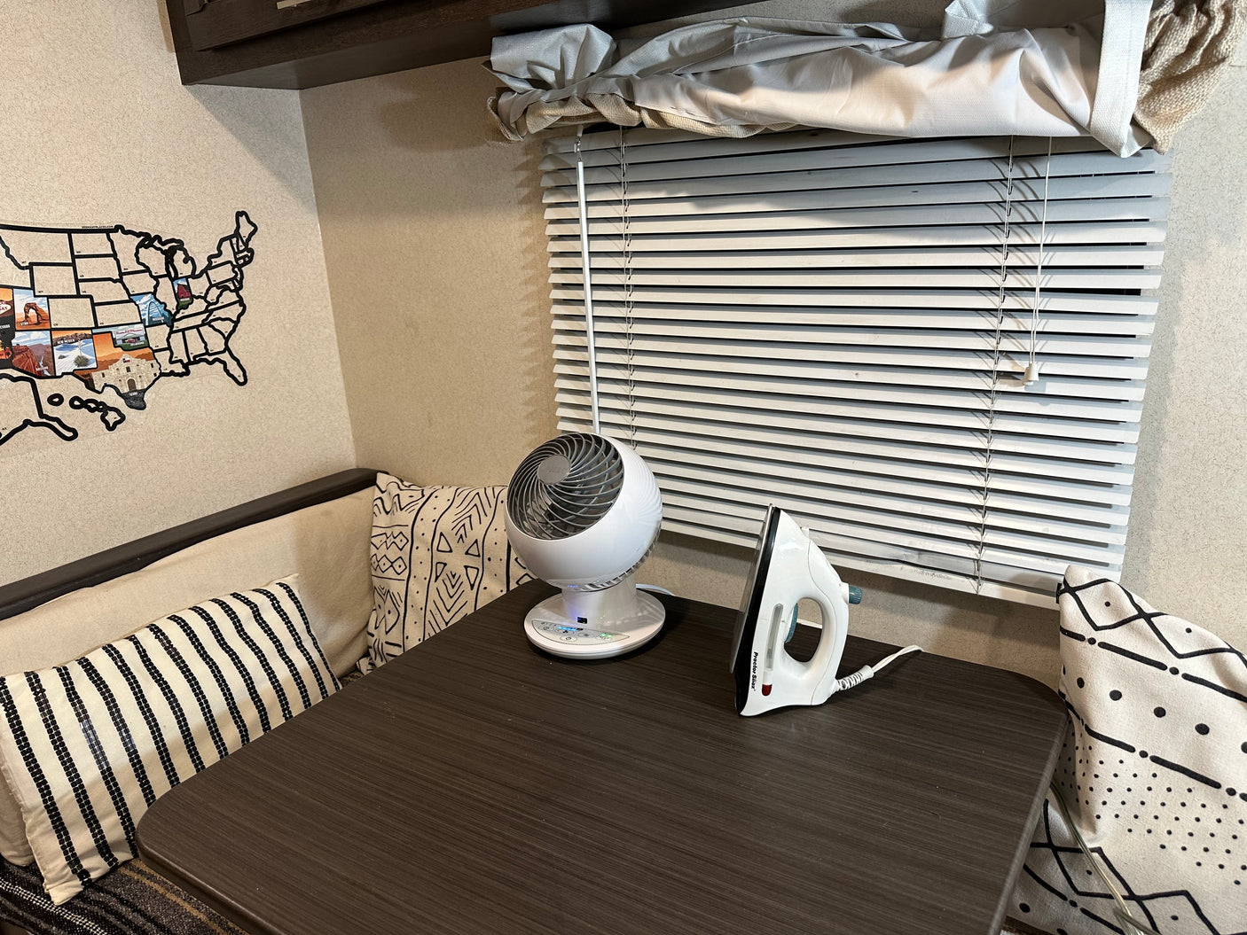 Cozy RV rental interior featuring a table with a small fan, an iron, decorative pillows, and a USA map on the wall.