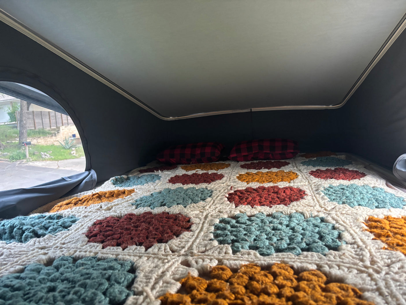 Cozy RV rental pop-top bed with colorful crochet blanket and plaid pillows, inviting comfort on the road.