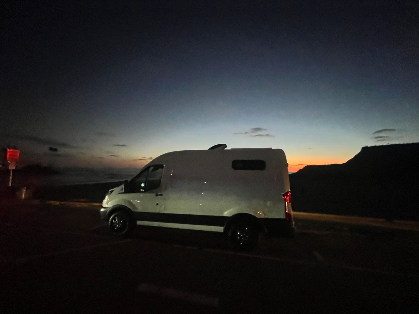 Scenic twilight view of an RV rental campervan parked by the ocean with distant mountains. Ready for adventure.