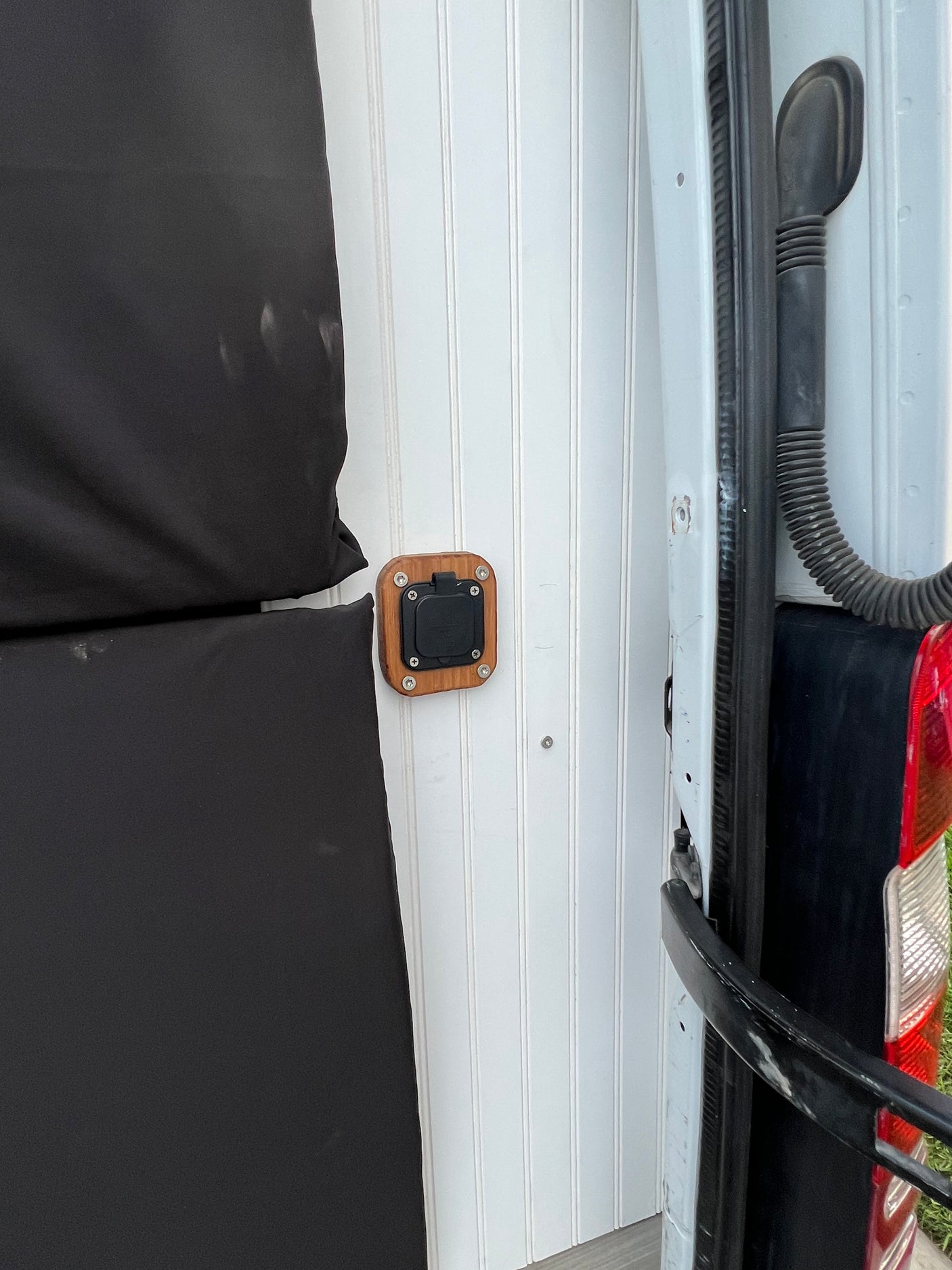 RV rental van interior showing black insulated panels, white beadboard, and a mounted power outlet near the rear.