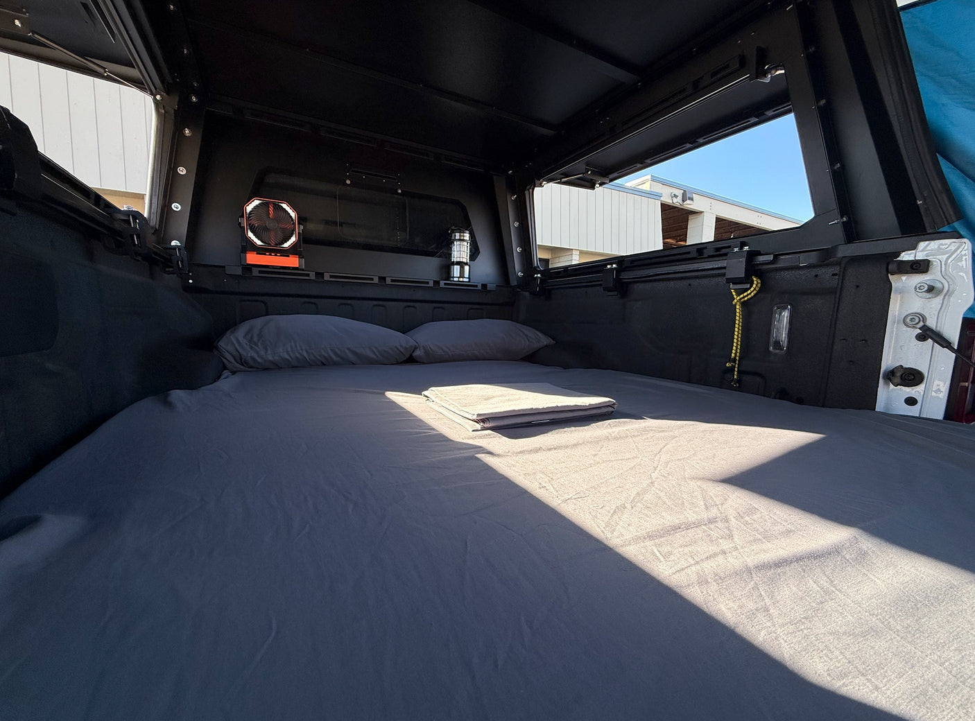 RV rental truck bed camping setup: cozy bed with pillows & sheet, fan, & lantern. Perfect for road trips!