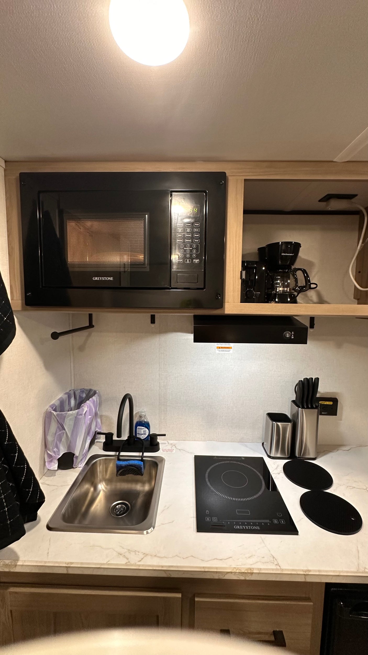 This RV rental features a well-equipped kitchen with a Greystone microwave, induction cooktop, sink, and coffee maker.