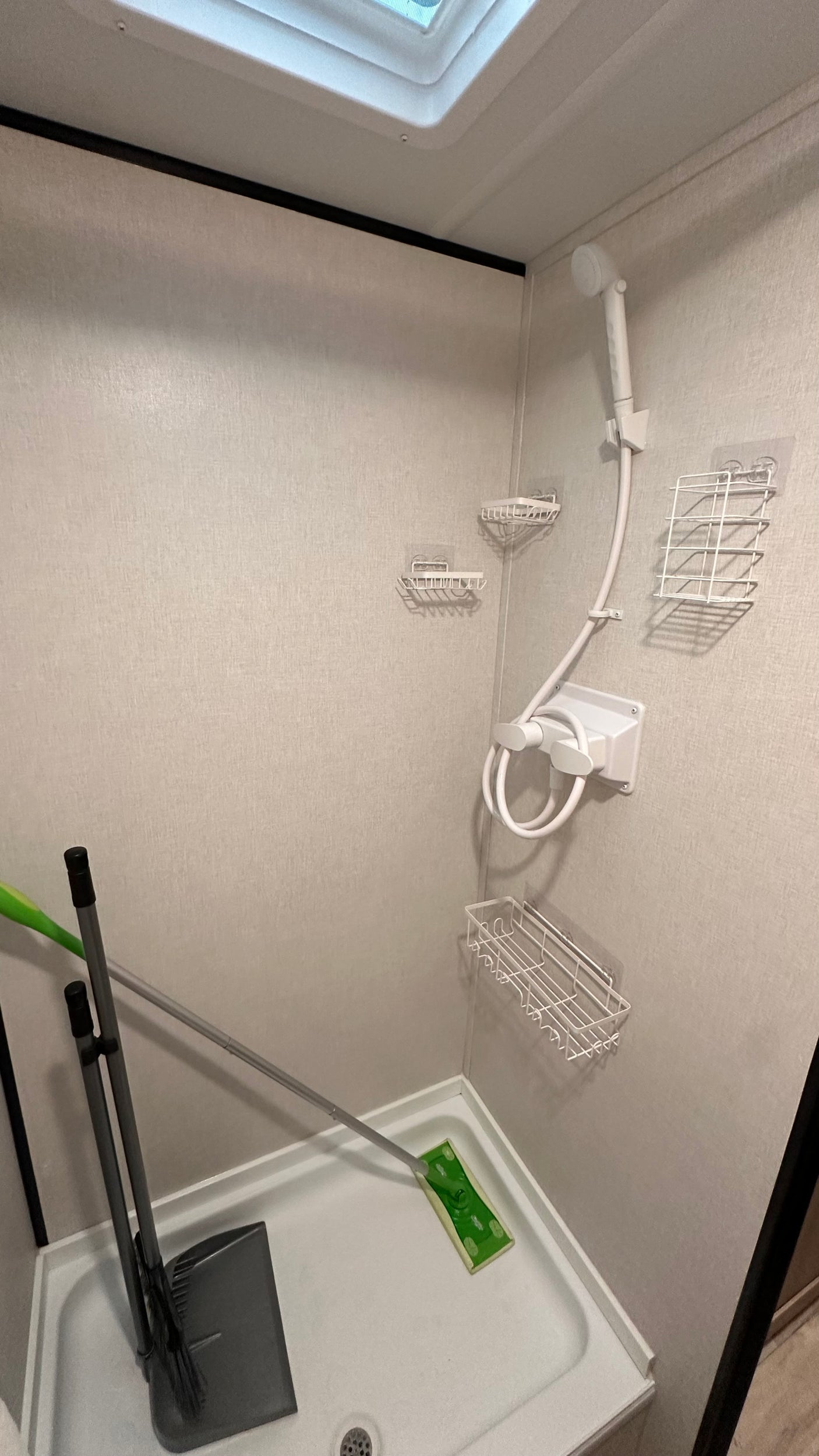 Inside an RV rental, this compact shower features a handheld shower head, wire caddies, and convenient storage for a broom and mop.