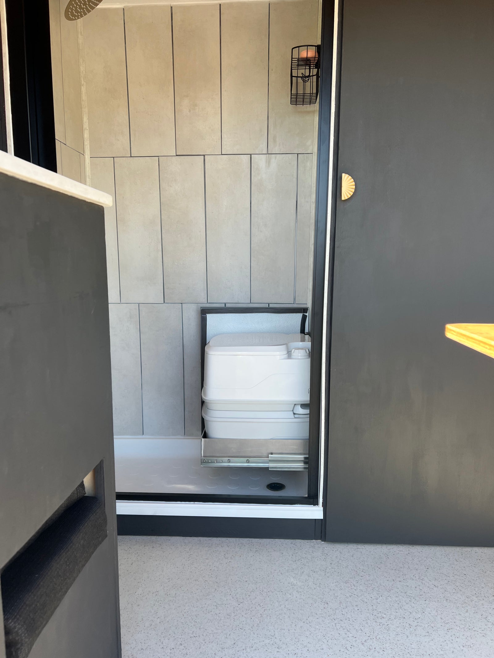 RV rental bathroom with modern grey tiles, shower, and space-saving pull-out portable toilet on sliders.