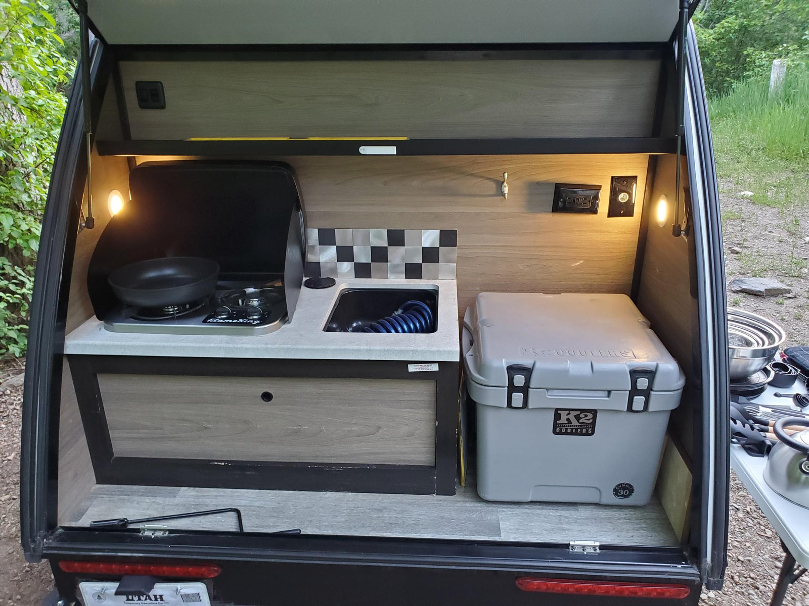 set up at a wooded campsite with a truck and fire pit.|Bushwhacker RV rental kitchen setup: camping pots