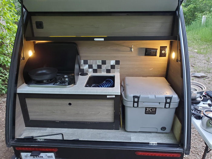 set up at a wooded campsite with a truck and fire pit.|Bushwhacker RV rental kitchen setup: camping pots