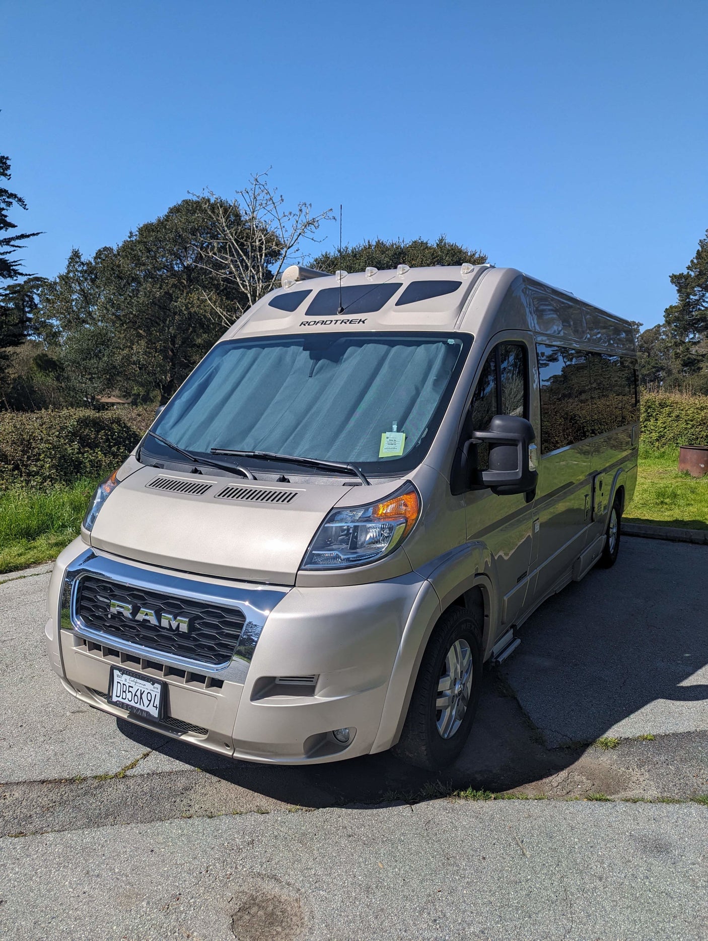 Sunny view of a beige Ram Roadtrek RV rental camper van parked on asphalt in nature.