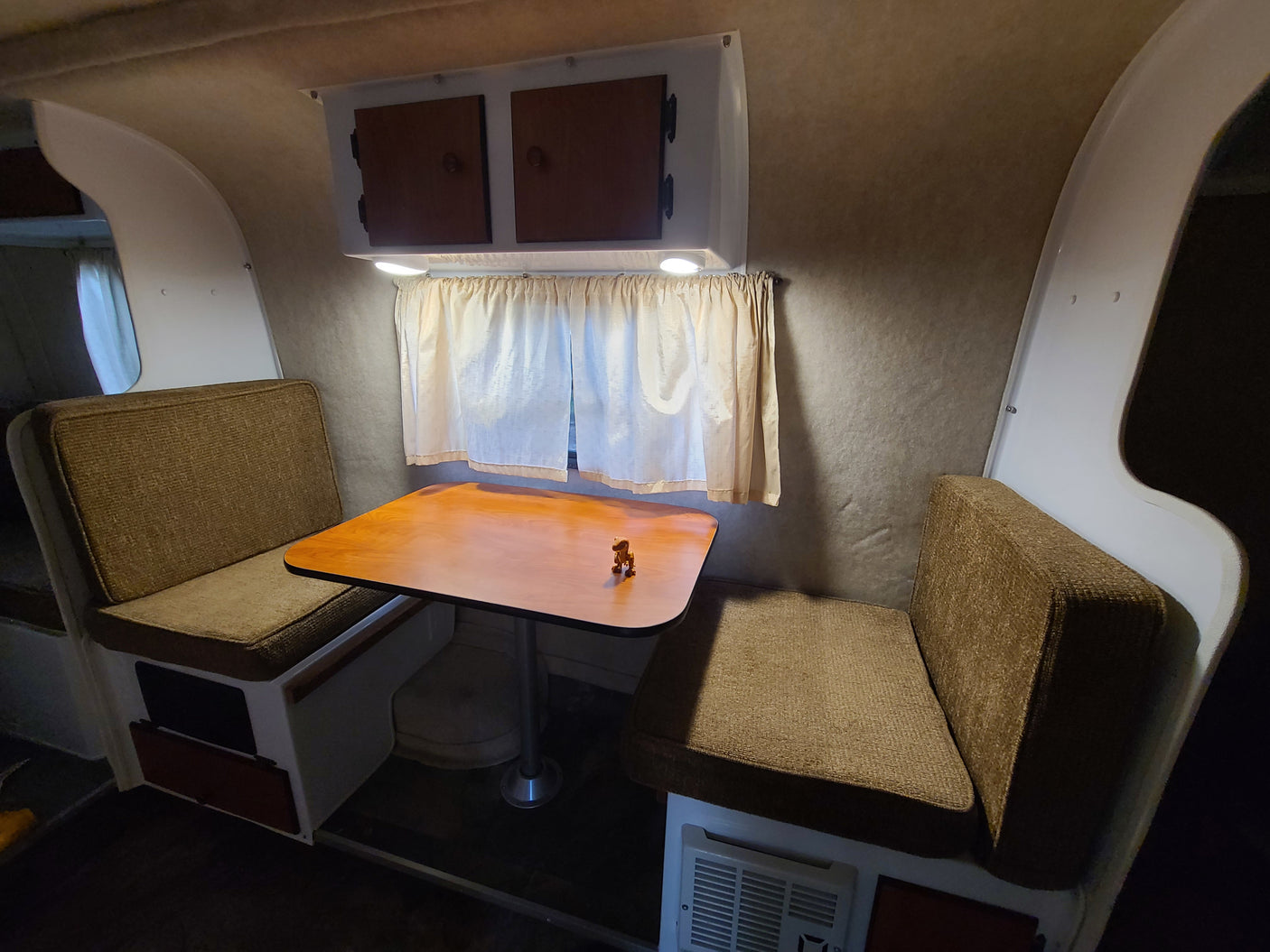 This RV rental features a cozy interior with a dinette, including two brown upholstered benches, a wooden table, and overhead cabinets.