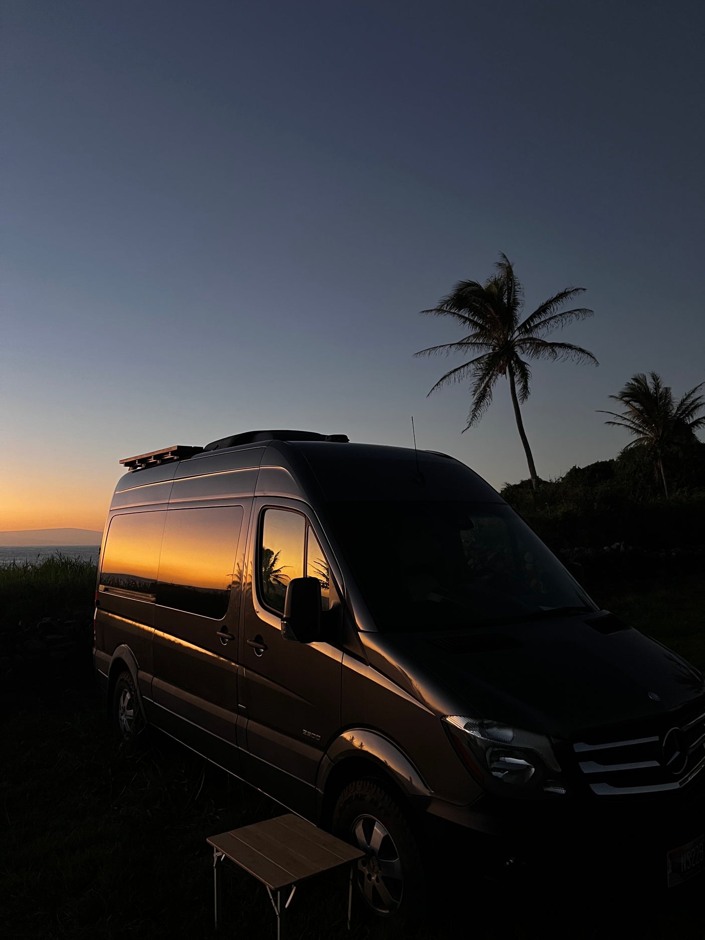 Golden sunset reflects beautifully on this Mercedes Sprinter **RV rental** van, parked near palm trees and the ocean.