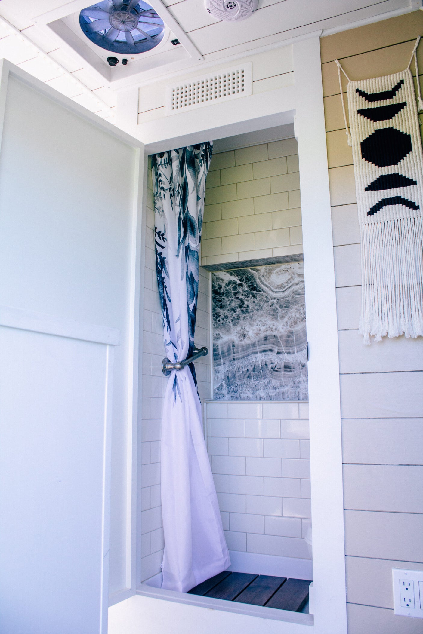 RV rental shower: modern design with subway tiles, unique marbled niche, leafy curtain, and ceiling fan for comfort.