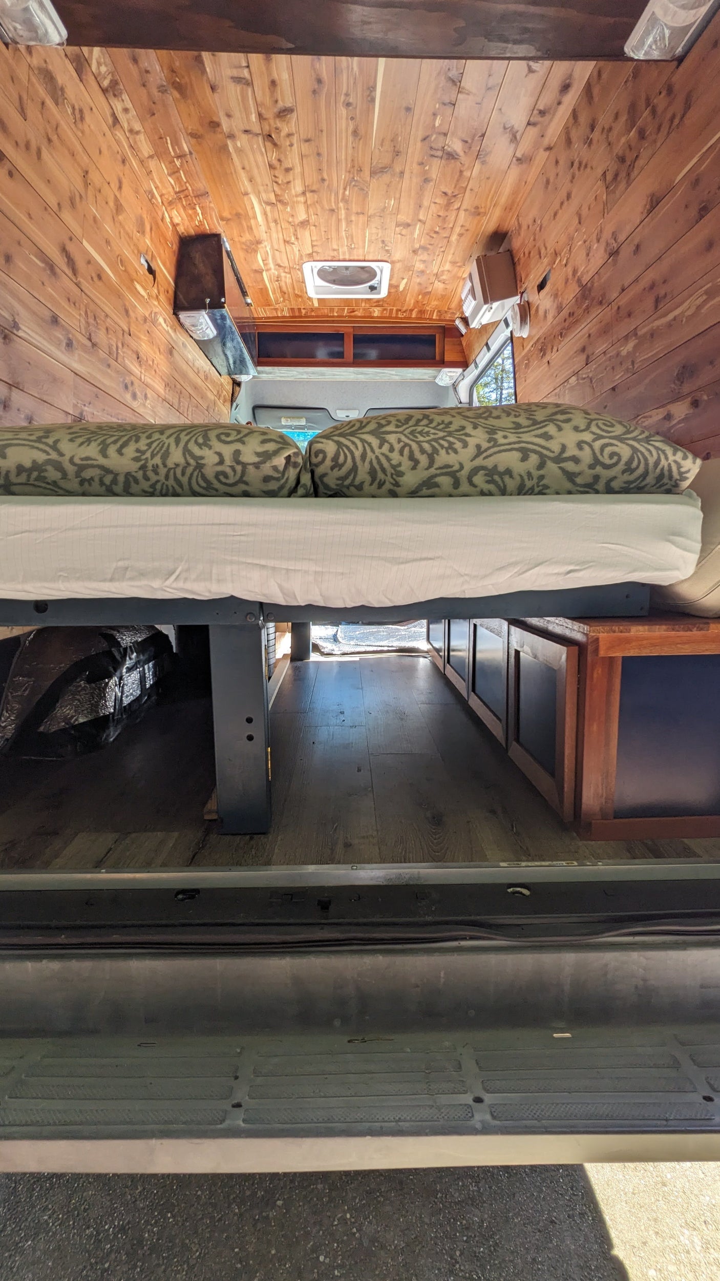 RV rental camper van interior: features wood paneling, an elevated bed with patterned pillows, and under-bed storage.