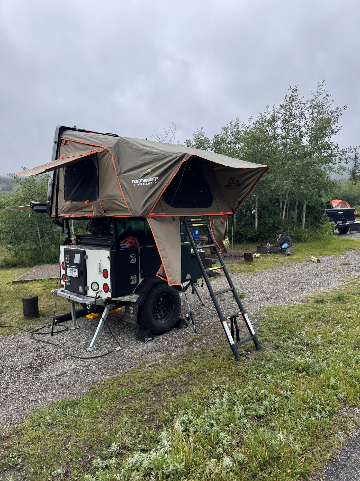 Experience overland camping with this RV rental! A gray trailer with olive rooftop tent and ladder, set up at a gravel site. — photo 9