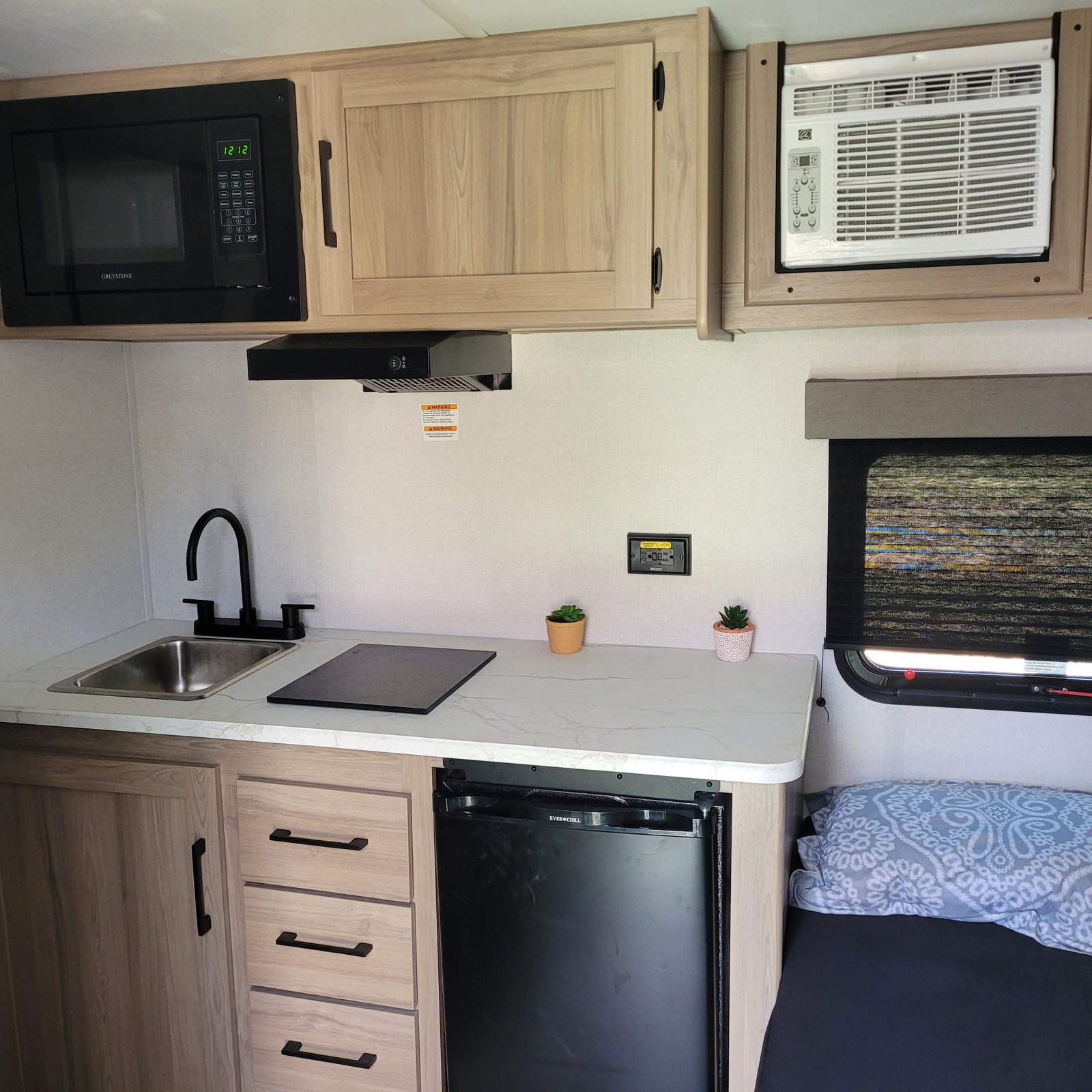 RV rental's compact kitchen. Includes microwave, sink, induction cooktop, mini-fridge, and AC unit, offering home comforts on the road.