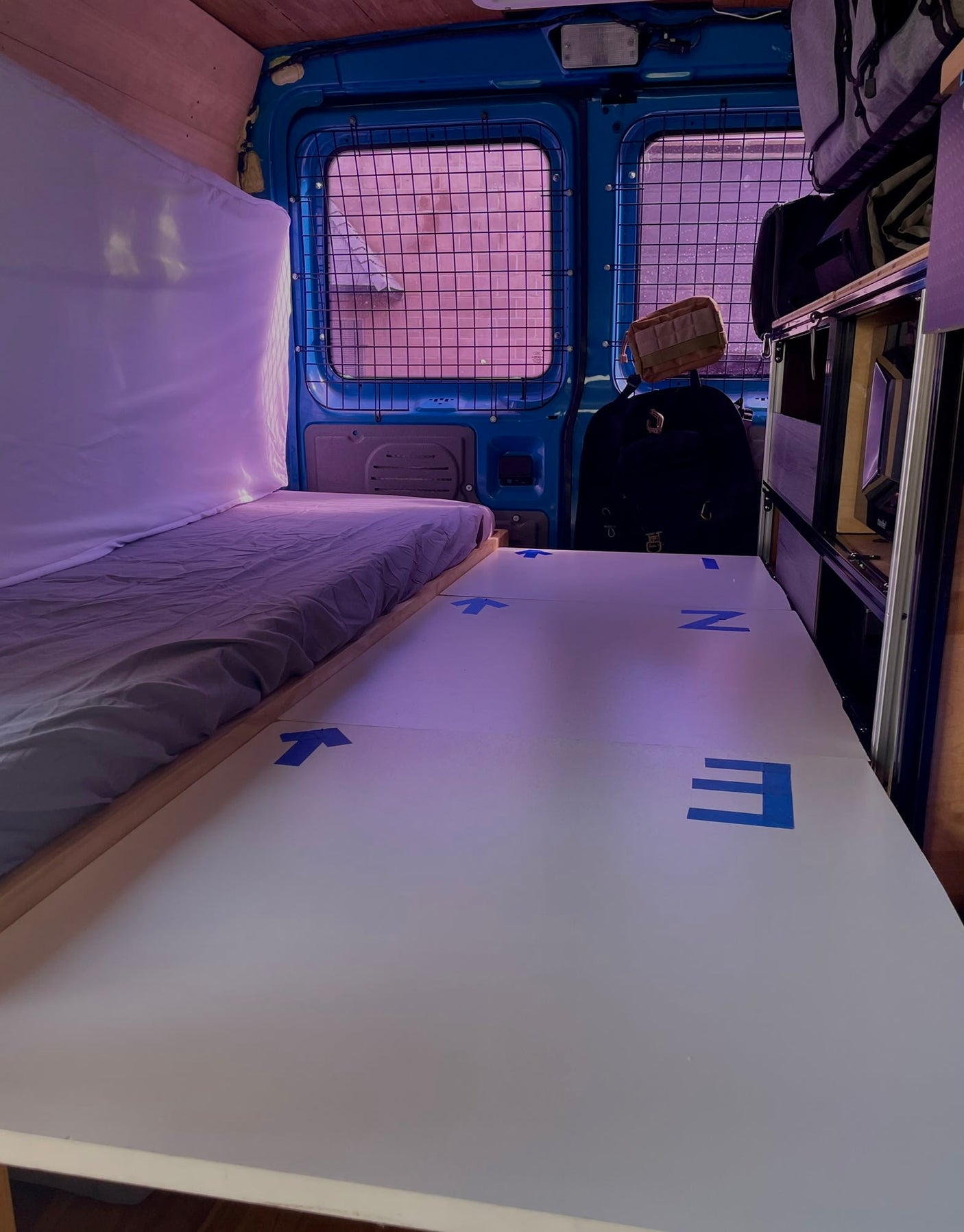 RV rental camper van interior: A cozy bed, white floor panels with blue tape, and built-in storage for your next adventure.