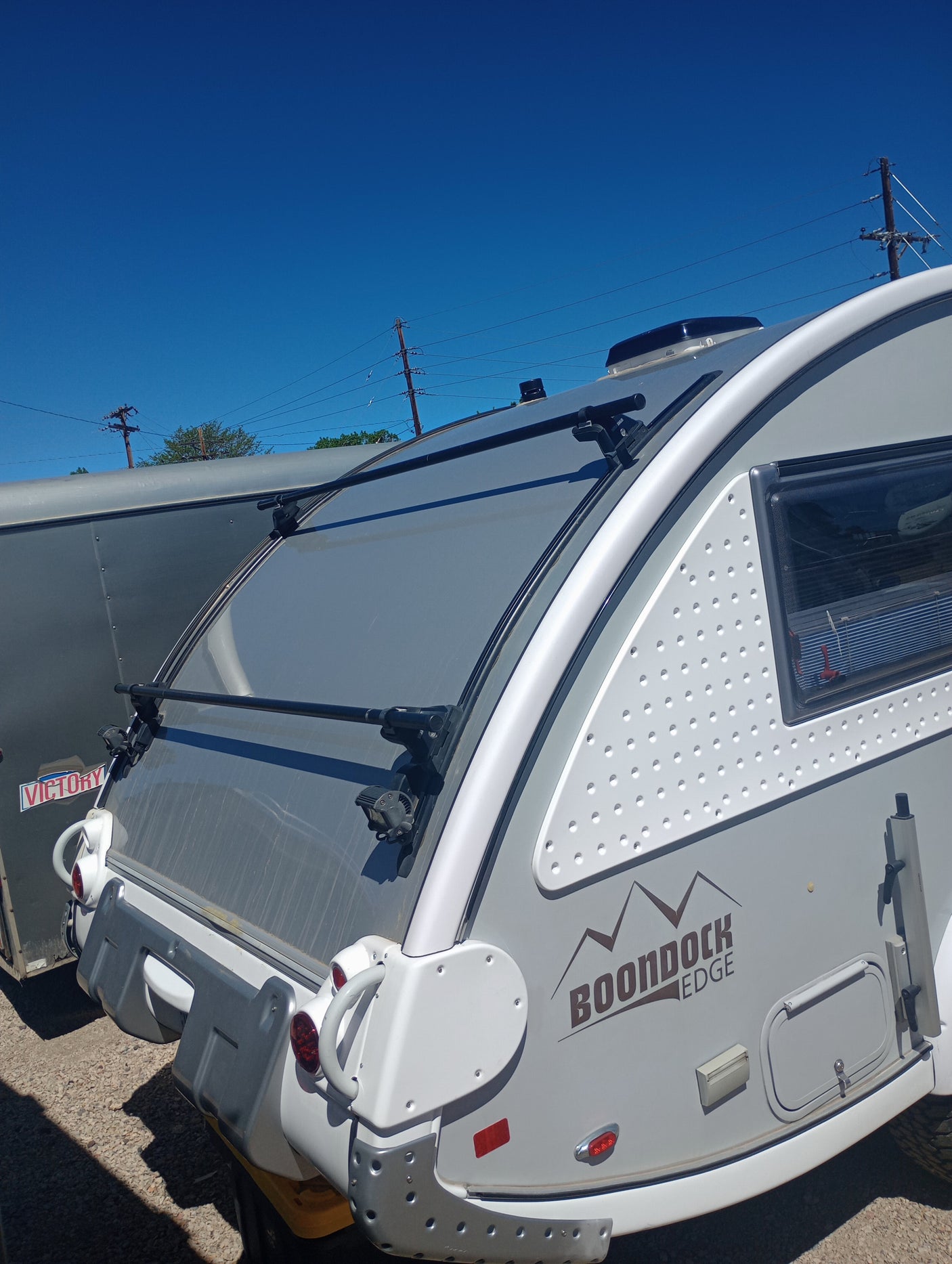 Boondock Edge teardrop RV rental, seen from the rear, with roof rack & modern design under a clear blue sky.