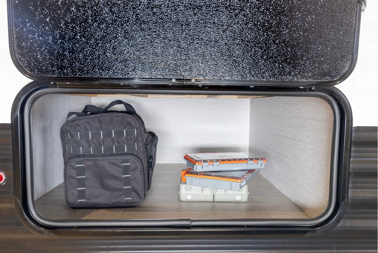 RV rental storage with a black utility bag and stacked organizer boxes inside a side compartment, ready for travel.