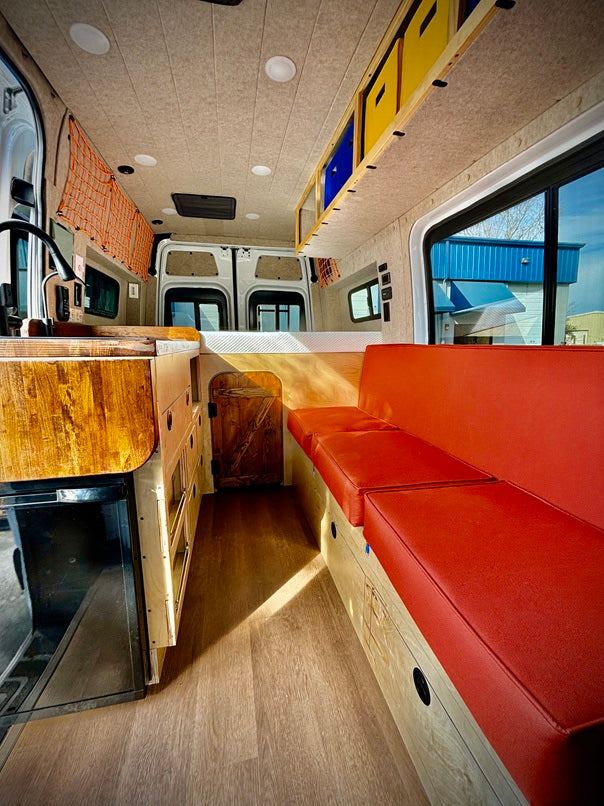 Step inside this modern RV rental! Features a compact kitchen, comfy red bench seating, and rear bed for mobile living.