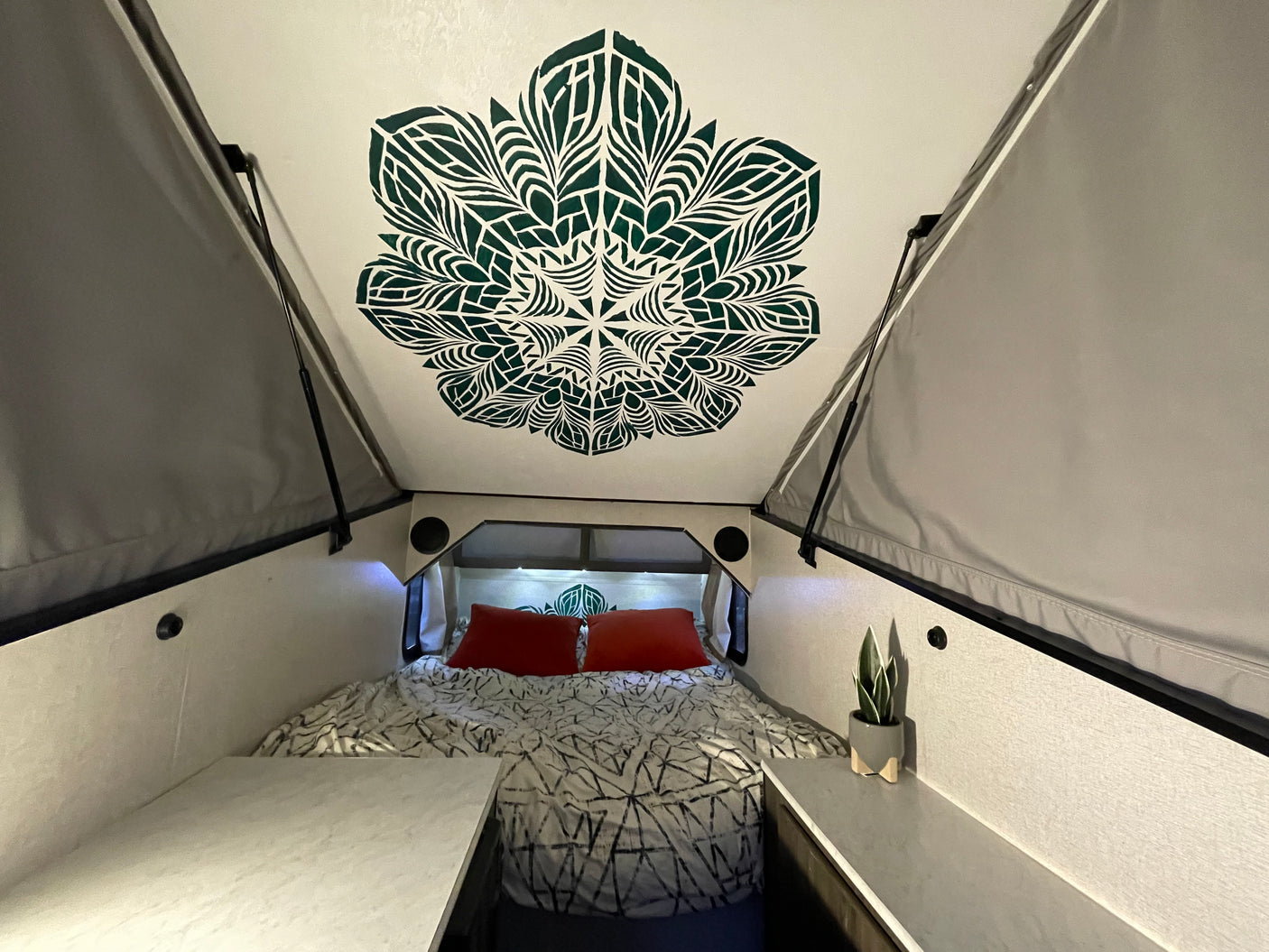 Cozy A-frame RV rental bedroom with a decorative mandala ceiling, comfy bed, and side storage.