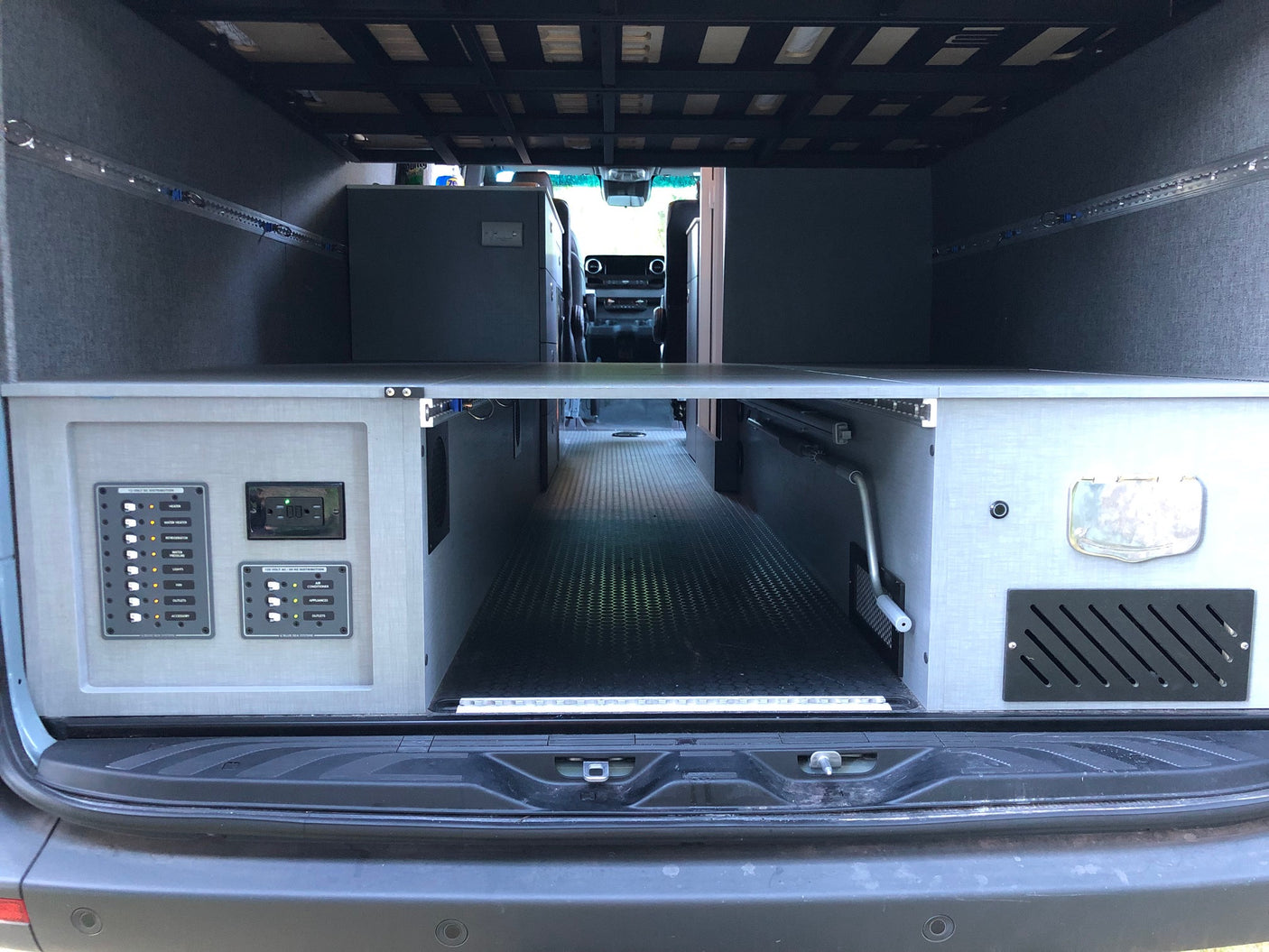 Rear interior of an RV rental camper van, showing under-bed storage, electrical controls, and a central aisle.