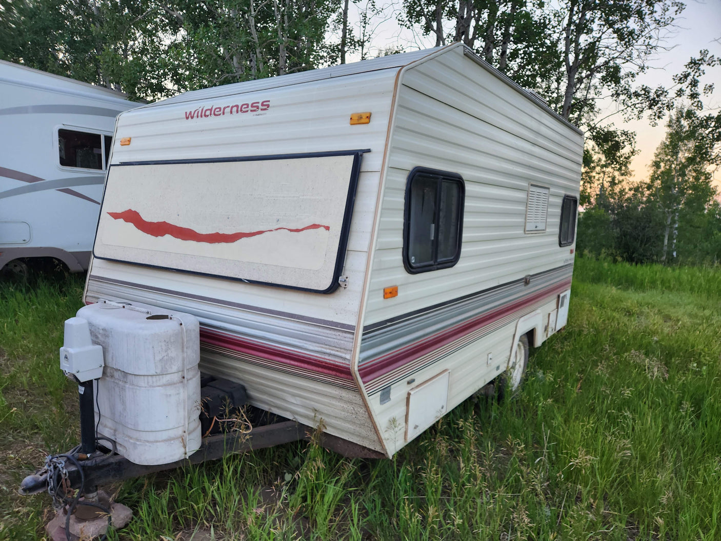 This white Wilderness travel trailer, with red & grey stripes, is parked in a grassy field. Perfect for an rv rental.