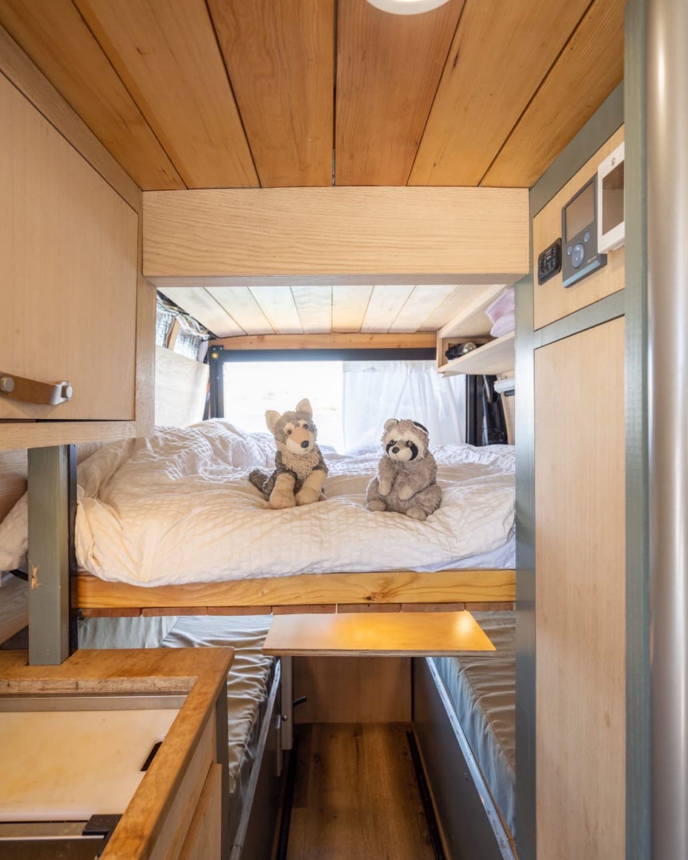 Explore this cozy RV rental interior: a raised bunk bed with plush toys, lower seating, and smart wood design for comfortable travel.
