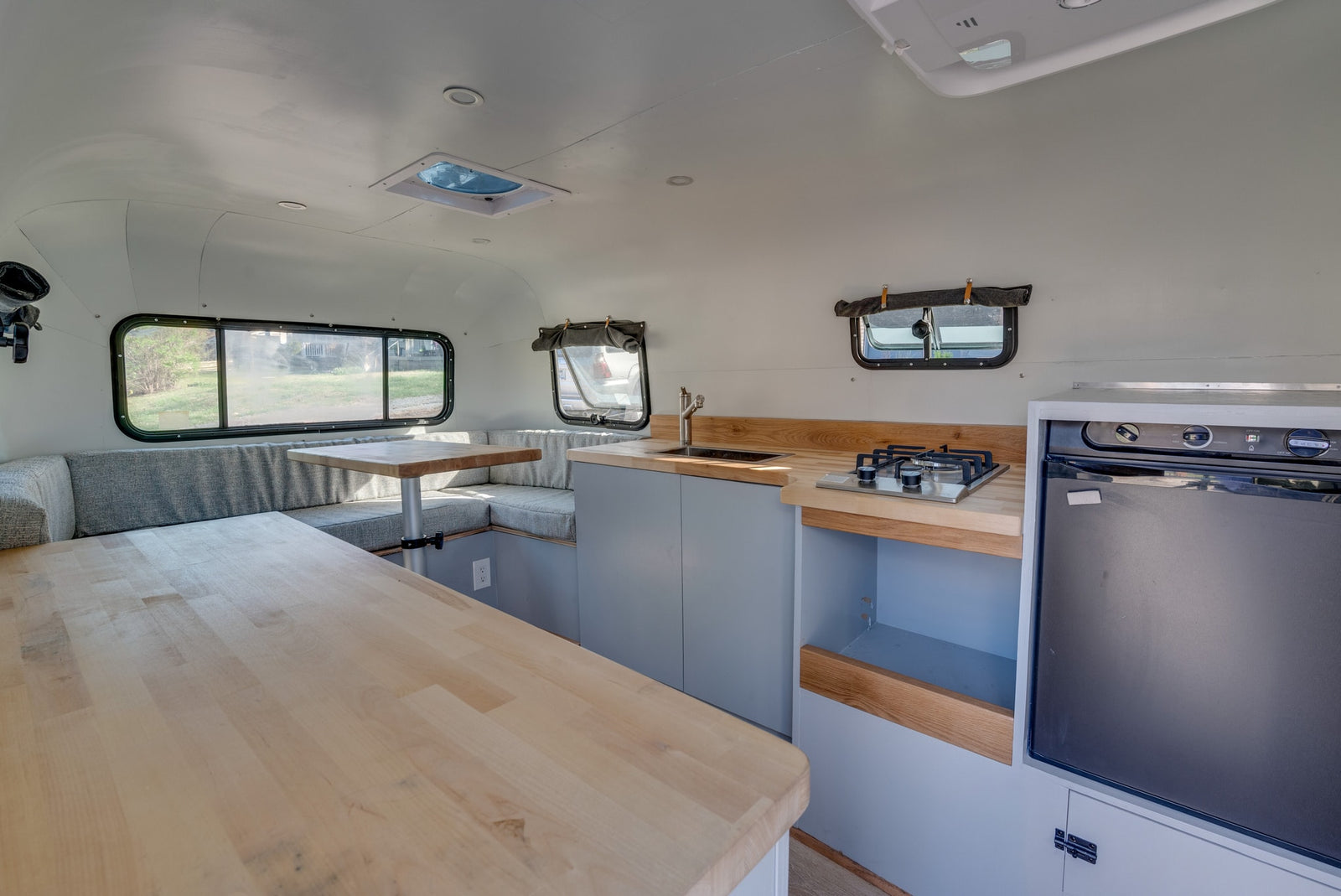 Well-appointed rv rental with light wood kitchen counters, sink, stove, fridge, and cozy gray dinette seating.