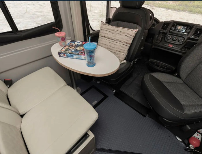 Inside this RV rental: a compact dining area with Clue game, soft seating, and the driver's cockpit beyond.