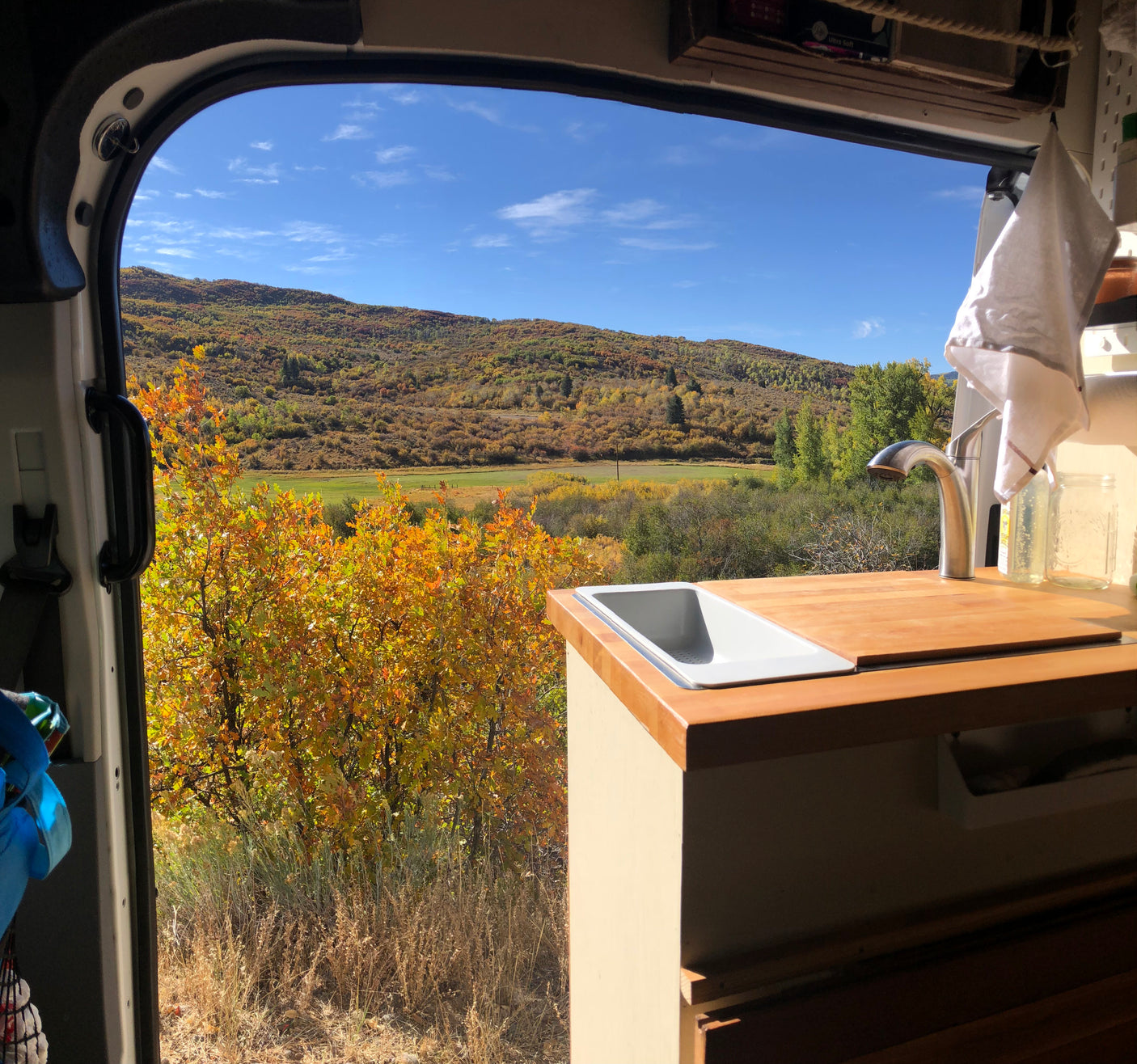 Serene RV rental view: cozy van kitchen with sink, faucet, overlooking autumn mountains & colorful foliage.