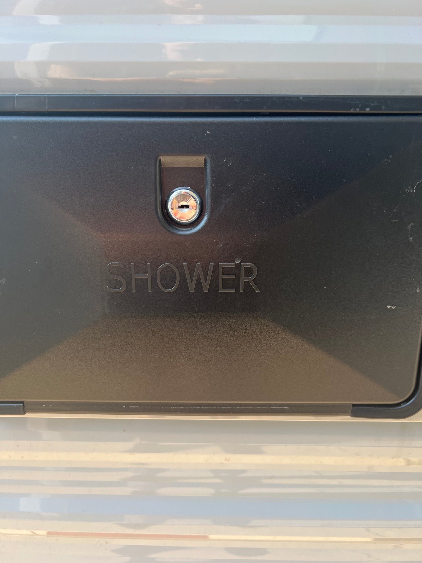 Close-up of an RV rental's black external shower compartment with a key lock, showing the "SHOWER" label.