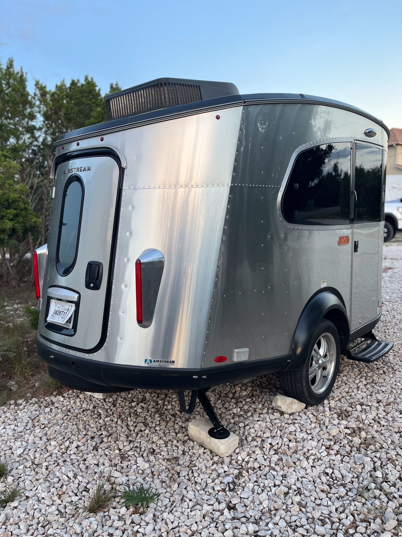 Stylish Airstream Basecamp travel trailer for an RV rental adventure, parked on gravel. Features sleek silver exterior & roof AC.