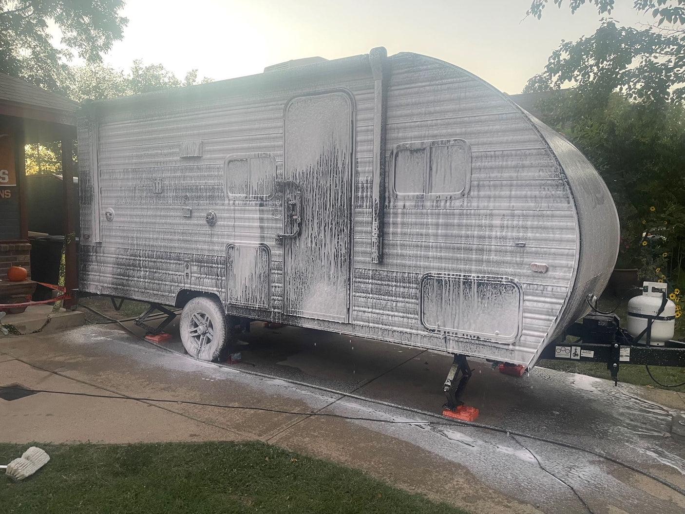 An RV rental covered in white soap suds during a wash on a driveway. Routine cleaning for adventurers.