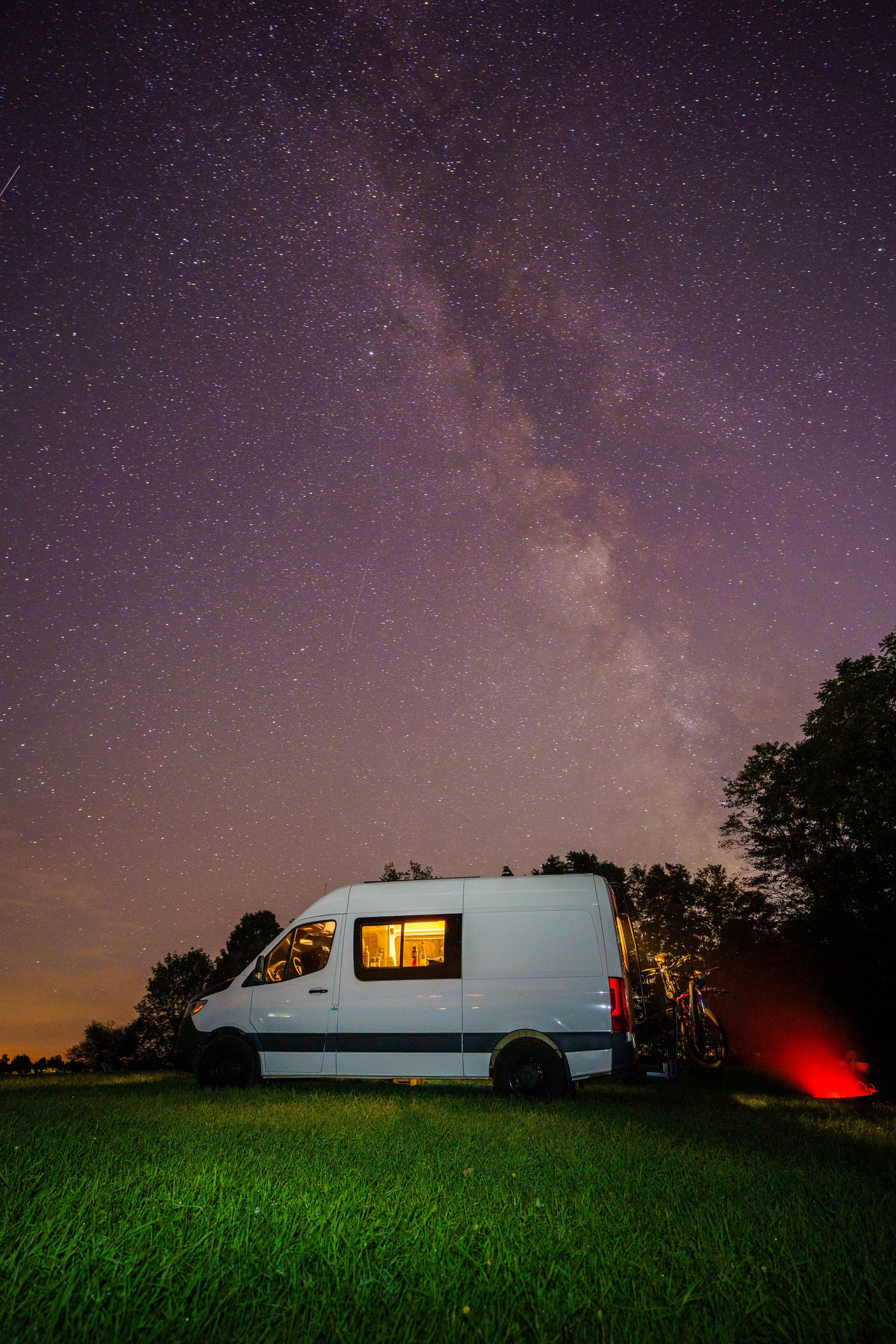 Cozy RV rental under a starry Milky Way sky in a grassy field. Perfect night camping adventure with bikes!