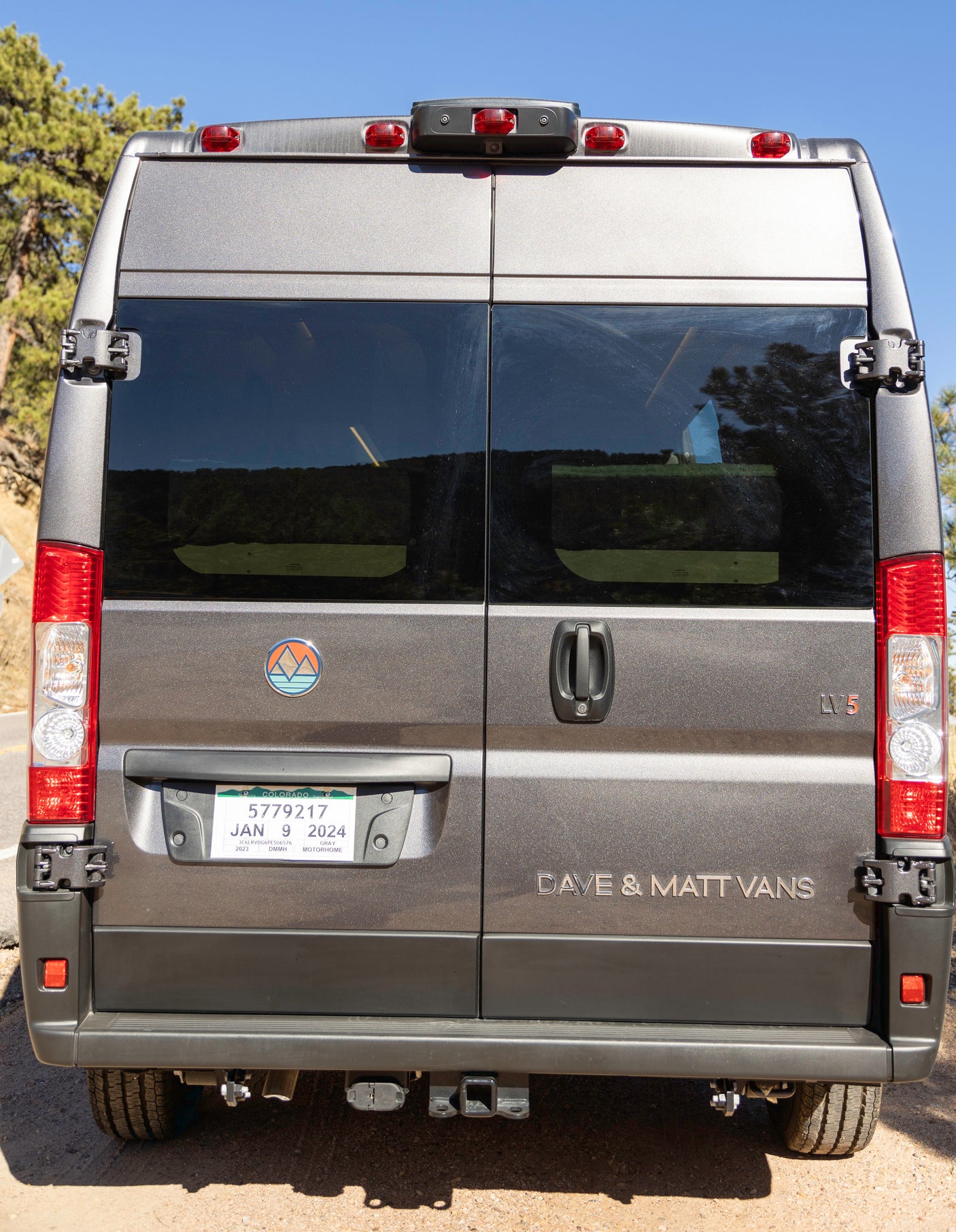 Rear view of a gray Colorado rv rental camper van, displaying its license plate, mountain logo, and "DAVE & MATT VANS" text.