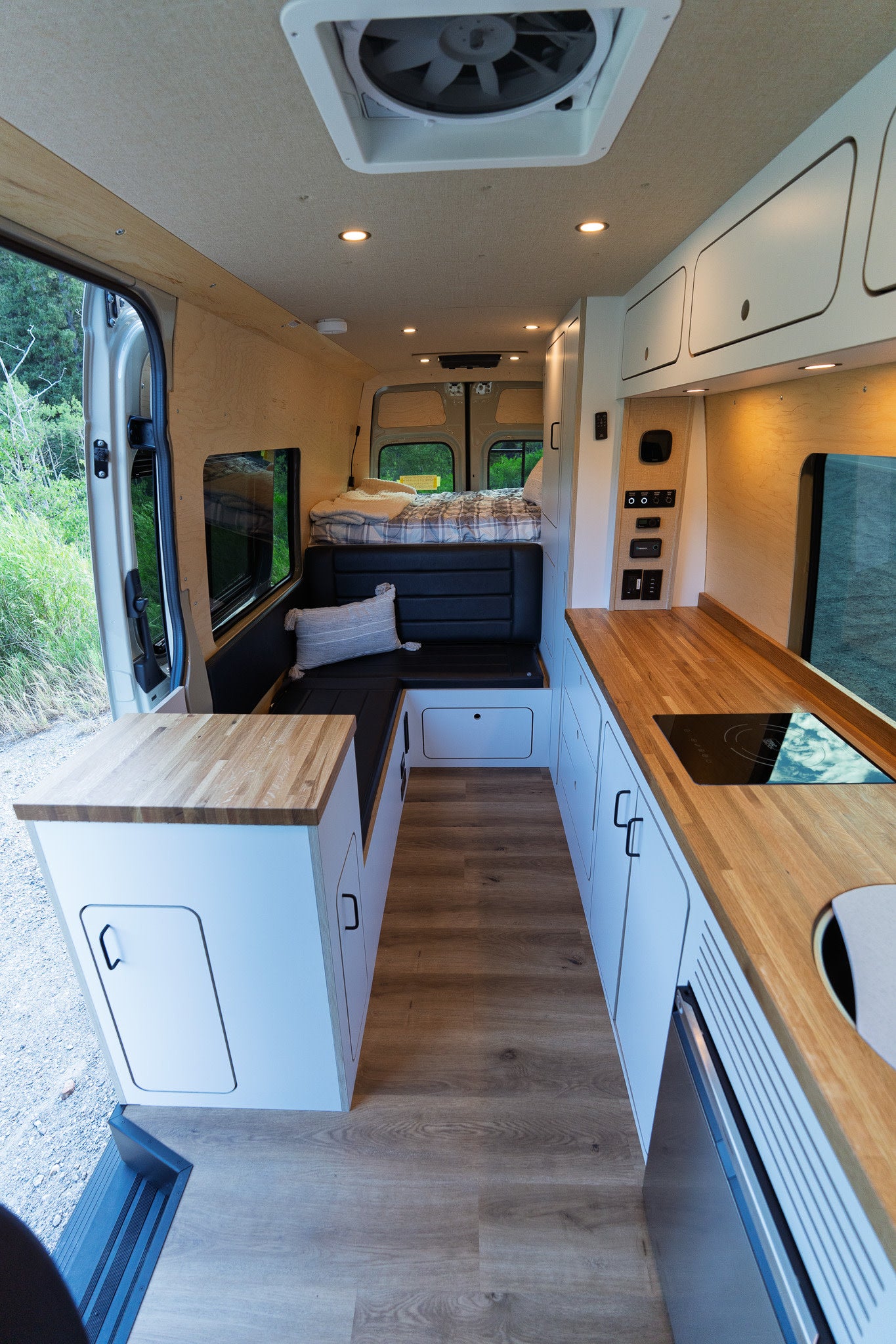 Bright, modern RV rental interior with wood accents, featuring a full kitchen, living area, and comfy bed.