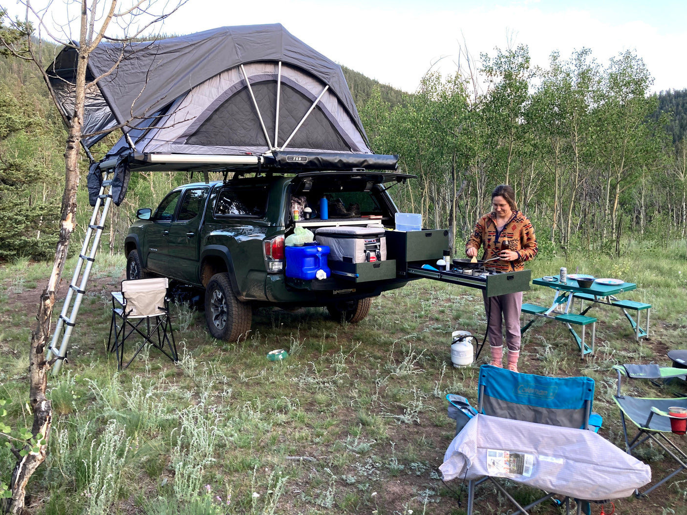 Your next RV rental adventure: a truck with a deployed rooftop tent and pull-out kitchen, perfect for outdoor camping.