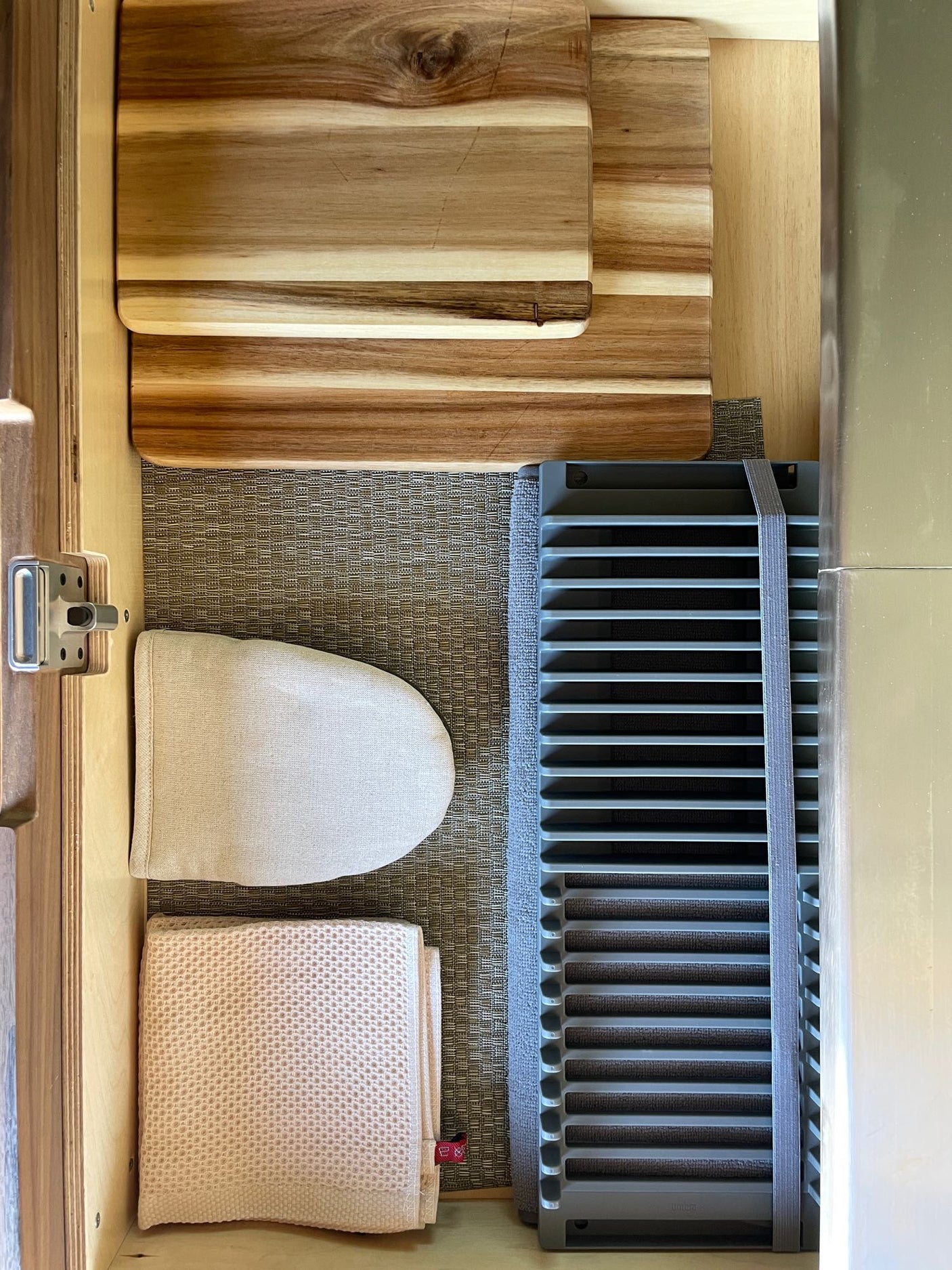 RV rental kitchen drawer: Organized wood cutting boards, hand ironing board, waffle towel, and slatted drying rack.