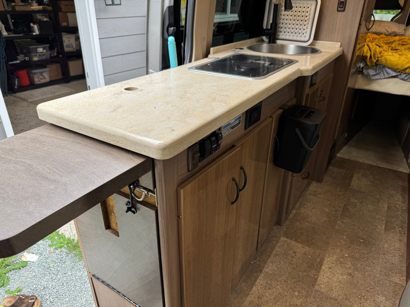 This rv rental interior features a compact kitchen with a sink, stovetop, extendable counter, and adjacent cozy bed.
