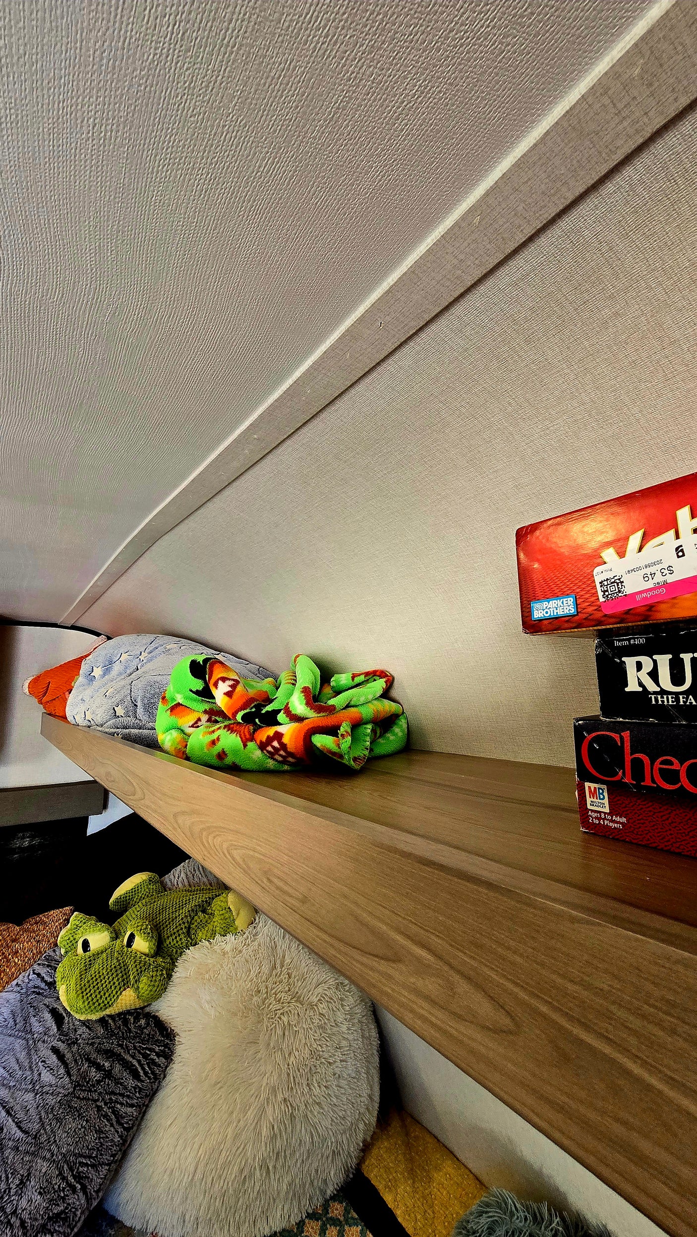 RV rental overhead shelf with games (Goodwill price tag visible), a colorful blanket, and plush toys in cozy storage.