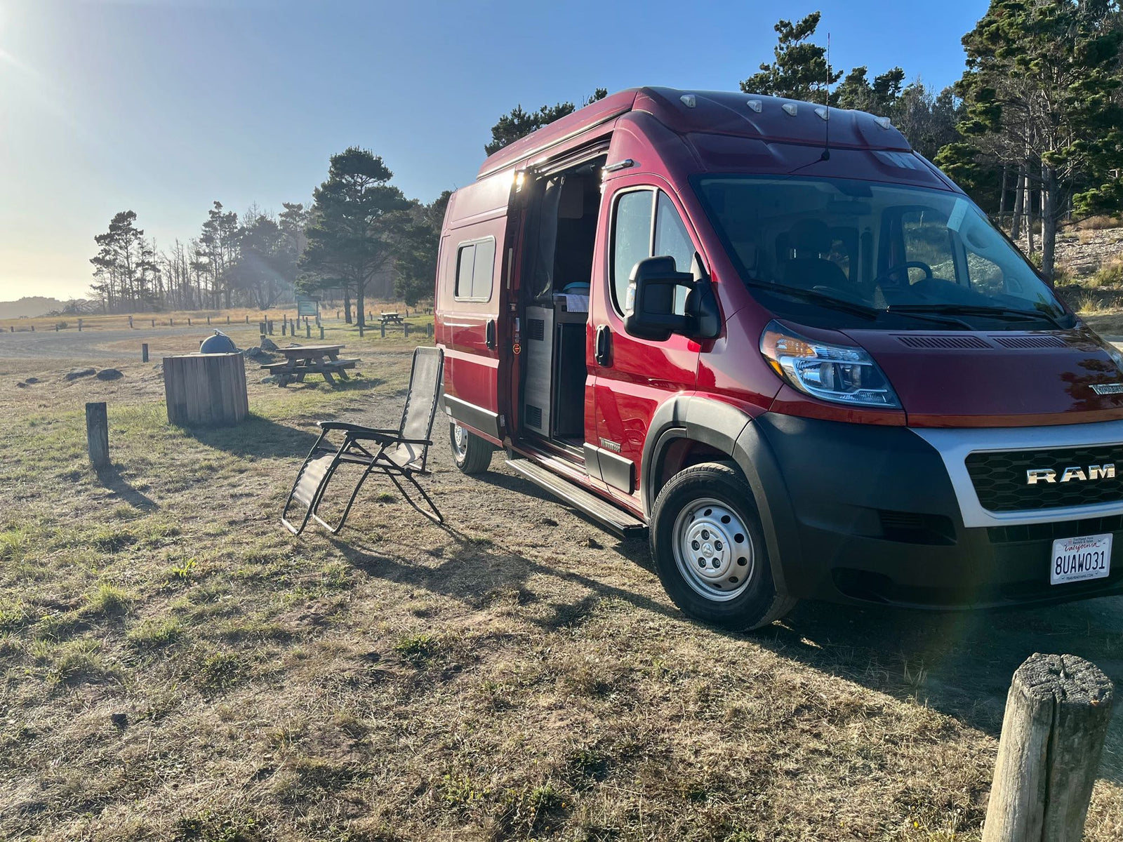 Enjoying a sunny day with an RV rental camper van parked in a scenic natural park. Chair set up outside.