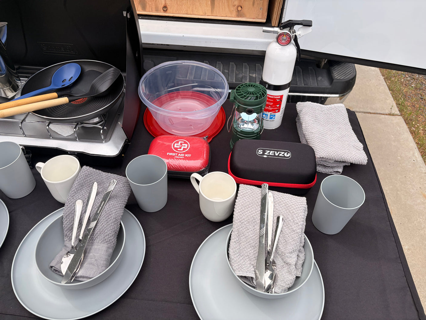 RV rental outdoor cooking & dining setup with a portable stove, pan, dishes, first aid, lantern, fire extinguisher.